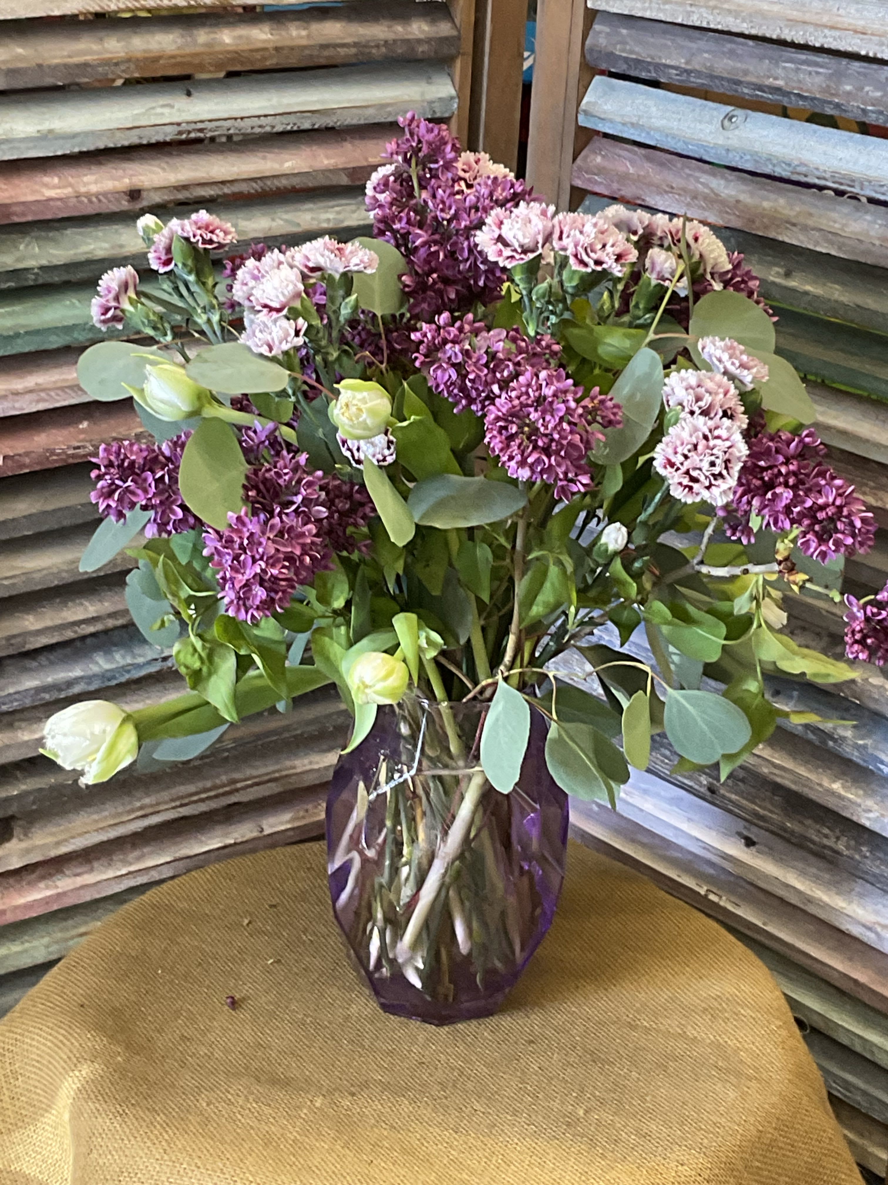 The Lilac Bouquet-26 - Clusters of purple lilac, pale pink mini carnations and white tulip buds arranged loosely in a deep purple glass vase.