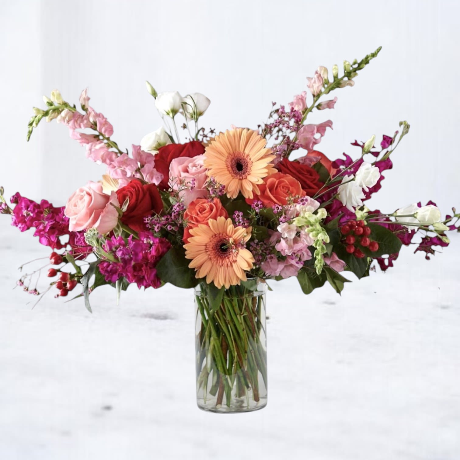 Studio Nerra - Studio Nerra is a modern garden-style arrangement designed with movement, texture, and effortless elegance in mind. Featuring a curated mix of premium seasonal blooms in soft blush, peach, coral, and vibrant berry tones, this piece blends romantic florals with fresh greenery for a look that feels both elevated and natural.  Designed in a clear glass vase with an airy, asymmetrical silhouette, Studio Nerra is perfect for everyday gifting, Mother’s Day, birthdays, or simply making a space feel beautifully styled.  Each Studio Nerra is handcrafted using the freshest blooms available and may include roses, gerbera daisies, stock, snapdragons, and specialty seasonal florals. Subtle variations make every arrangement one-of-a-kind while preserving the overall color palette and design aesthetic.