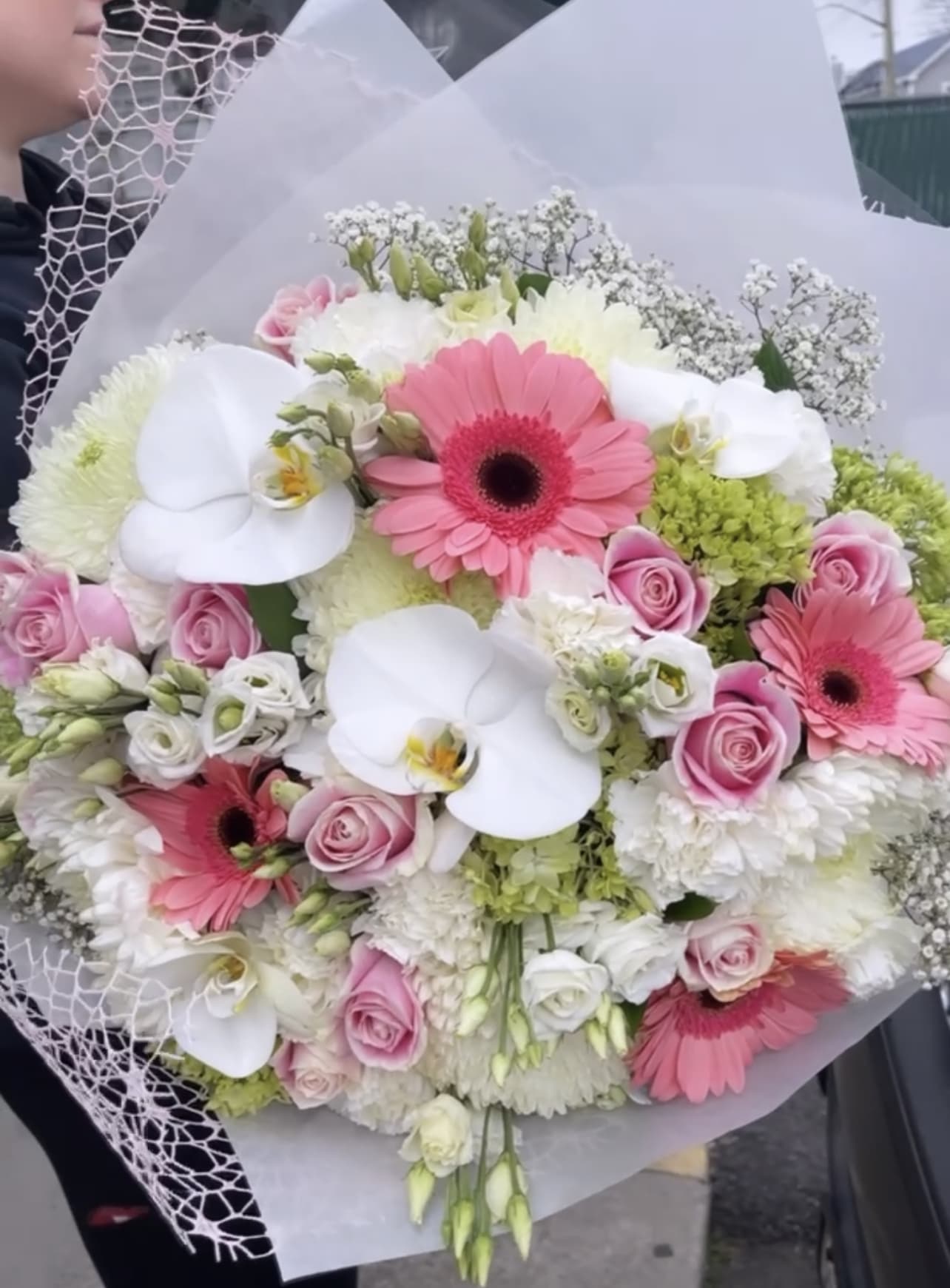 Handheld bouquet of pink gerberas, white orchids, and roses wrapped in white paper