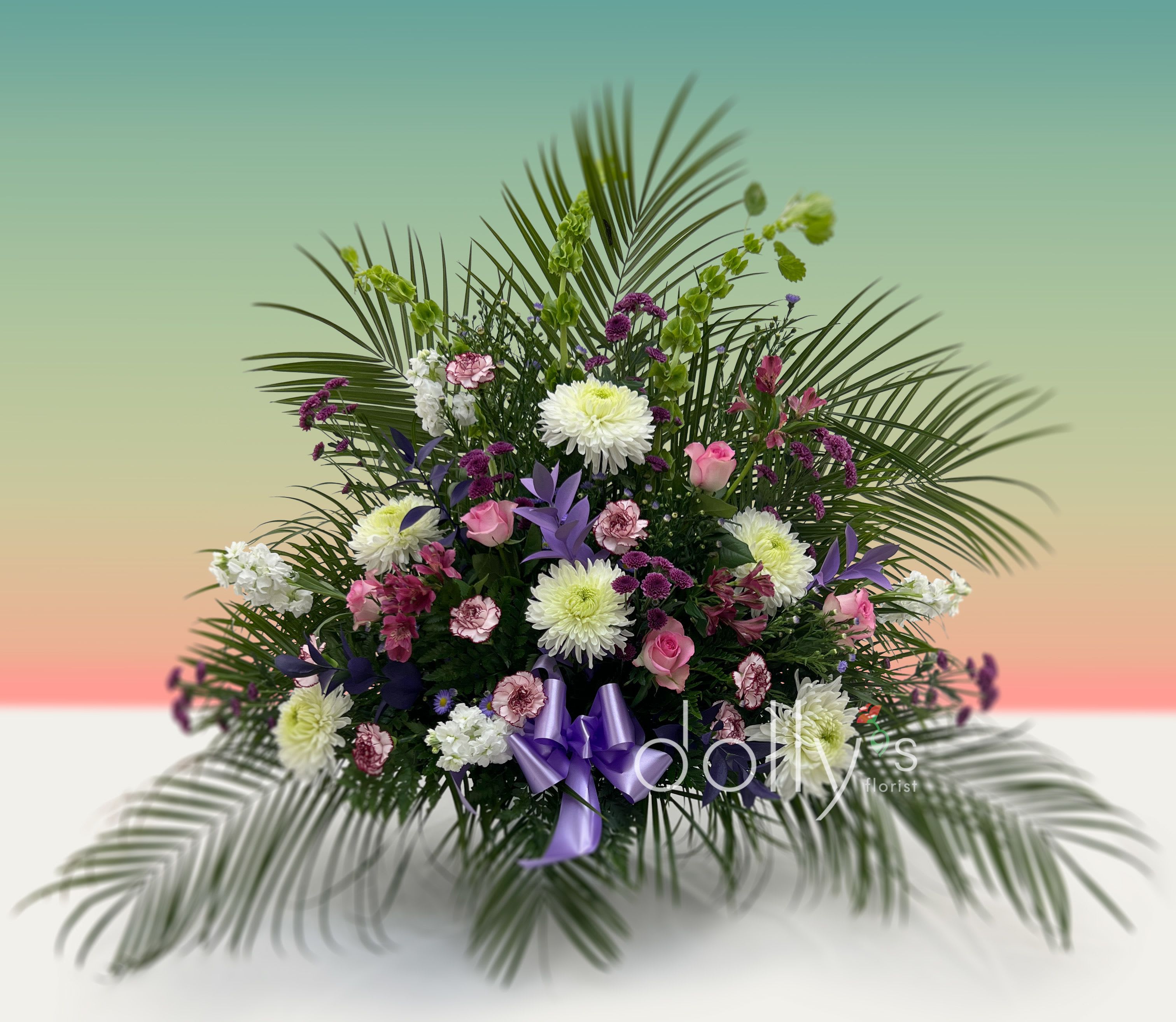 Large floral arrangement with pink, white, and purple flowers and palm fronds
