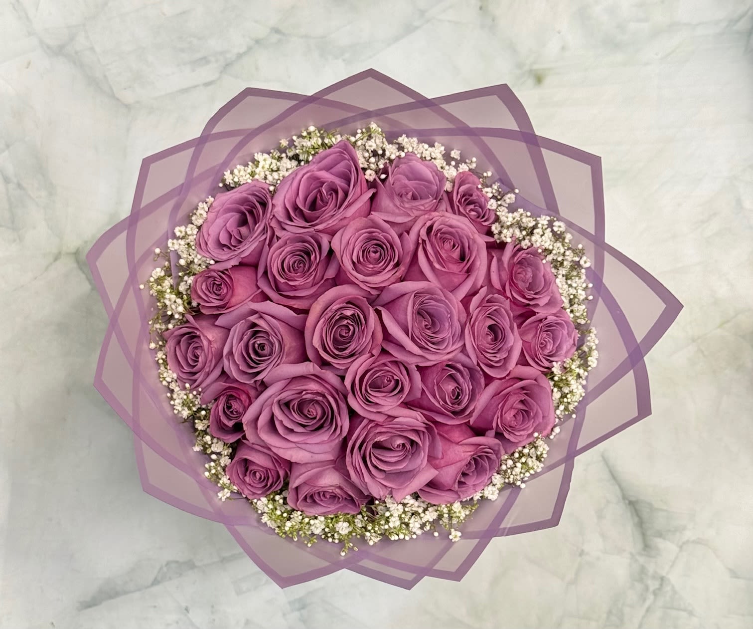 Round bouquet of purple roses with white filler flowers wrapped in lavender paper