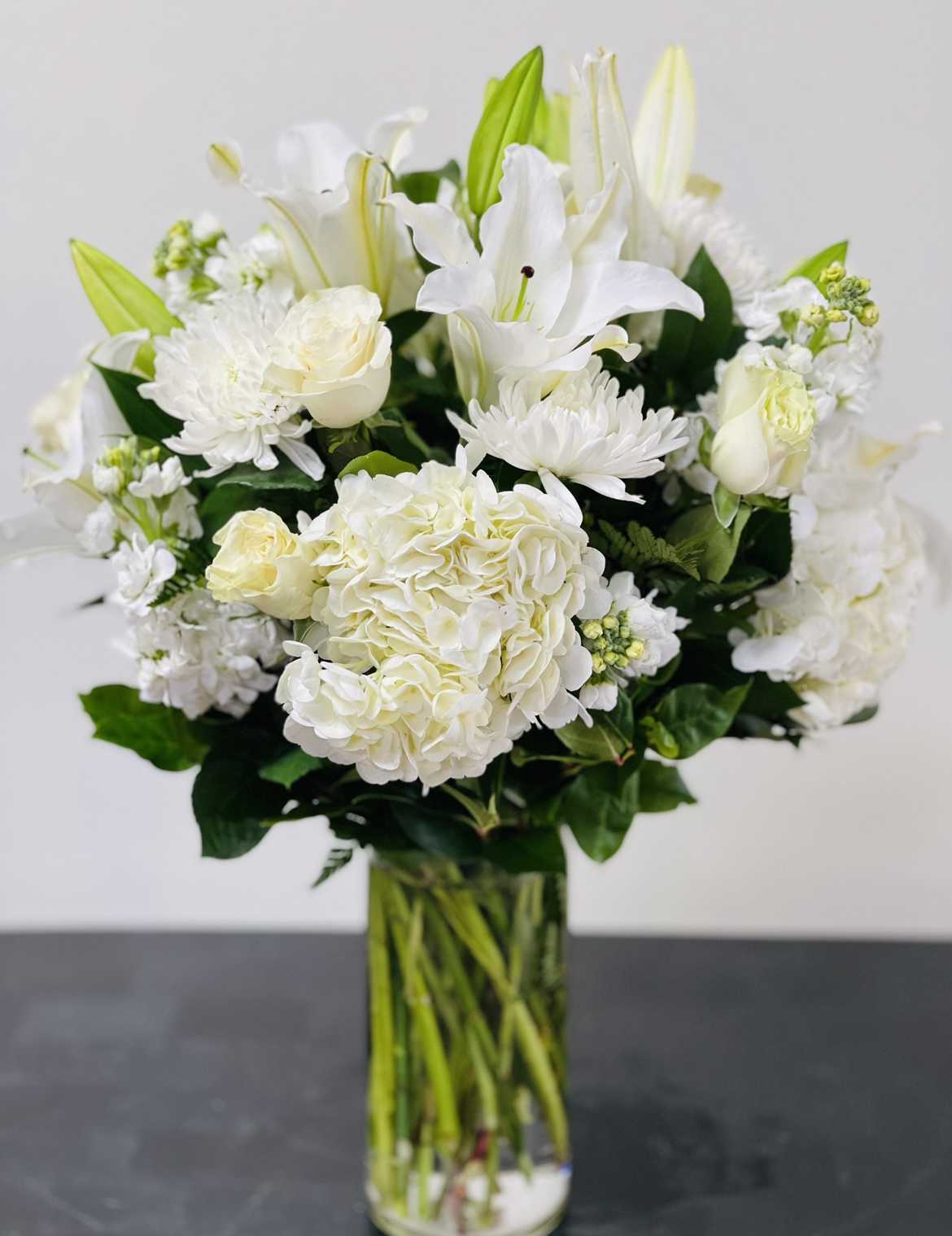 White lilies and roses arranged in a clear glass vase