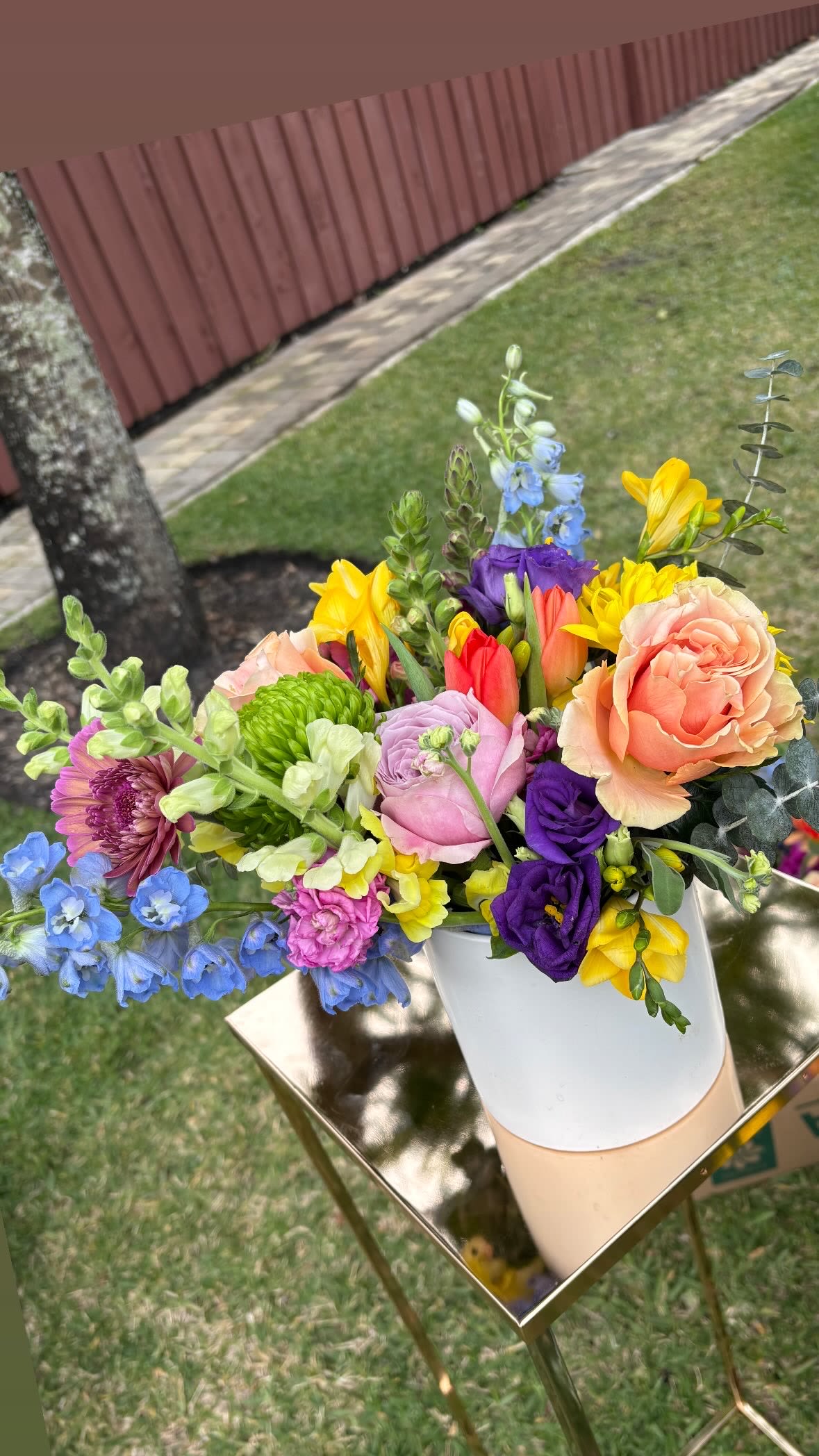 Colorful mixed bouquet in a white vase on a gold stand.