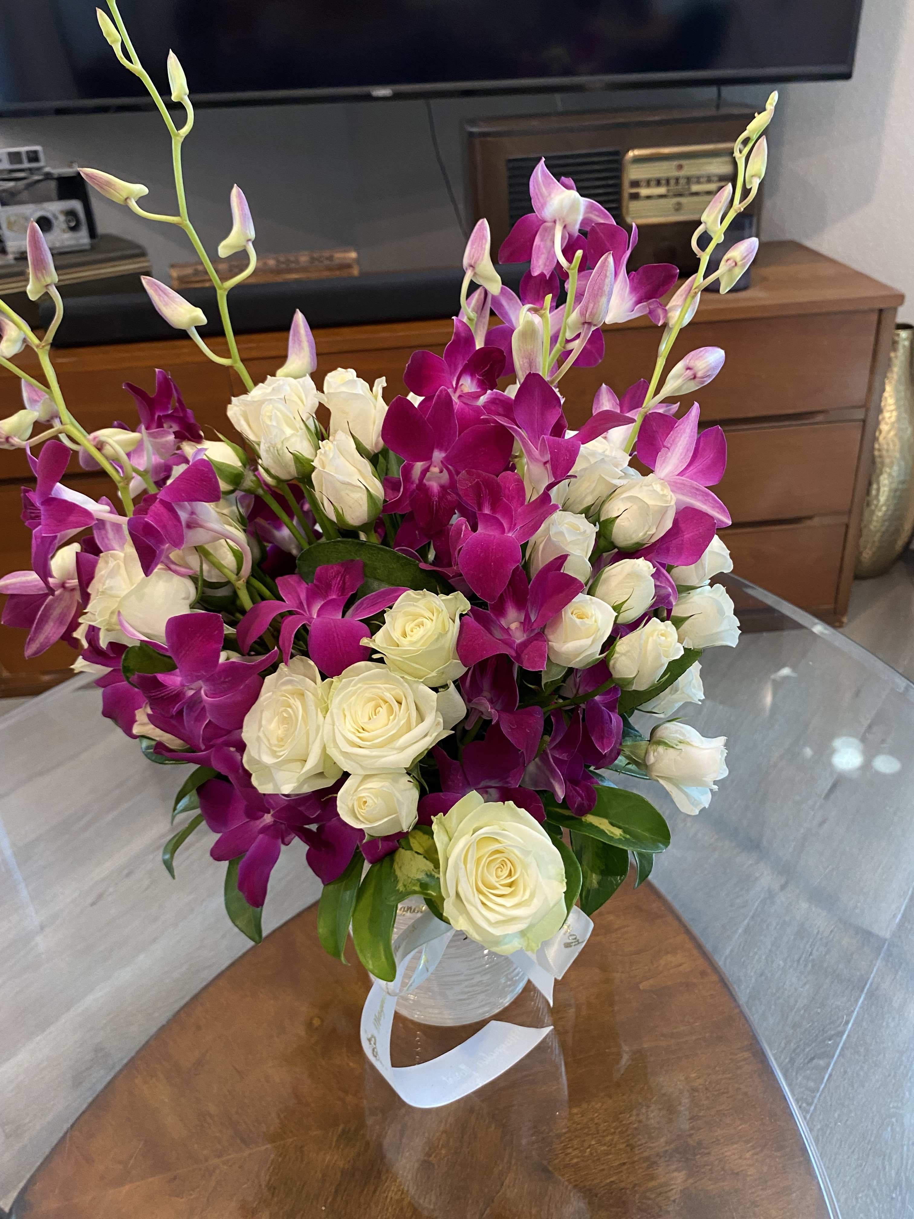 Bouquet of white roses and magenta orchids in a clear vase