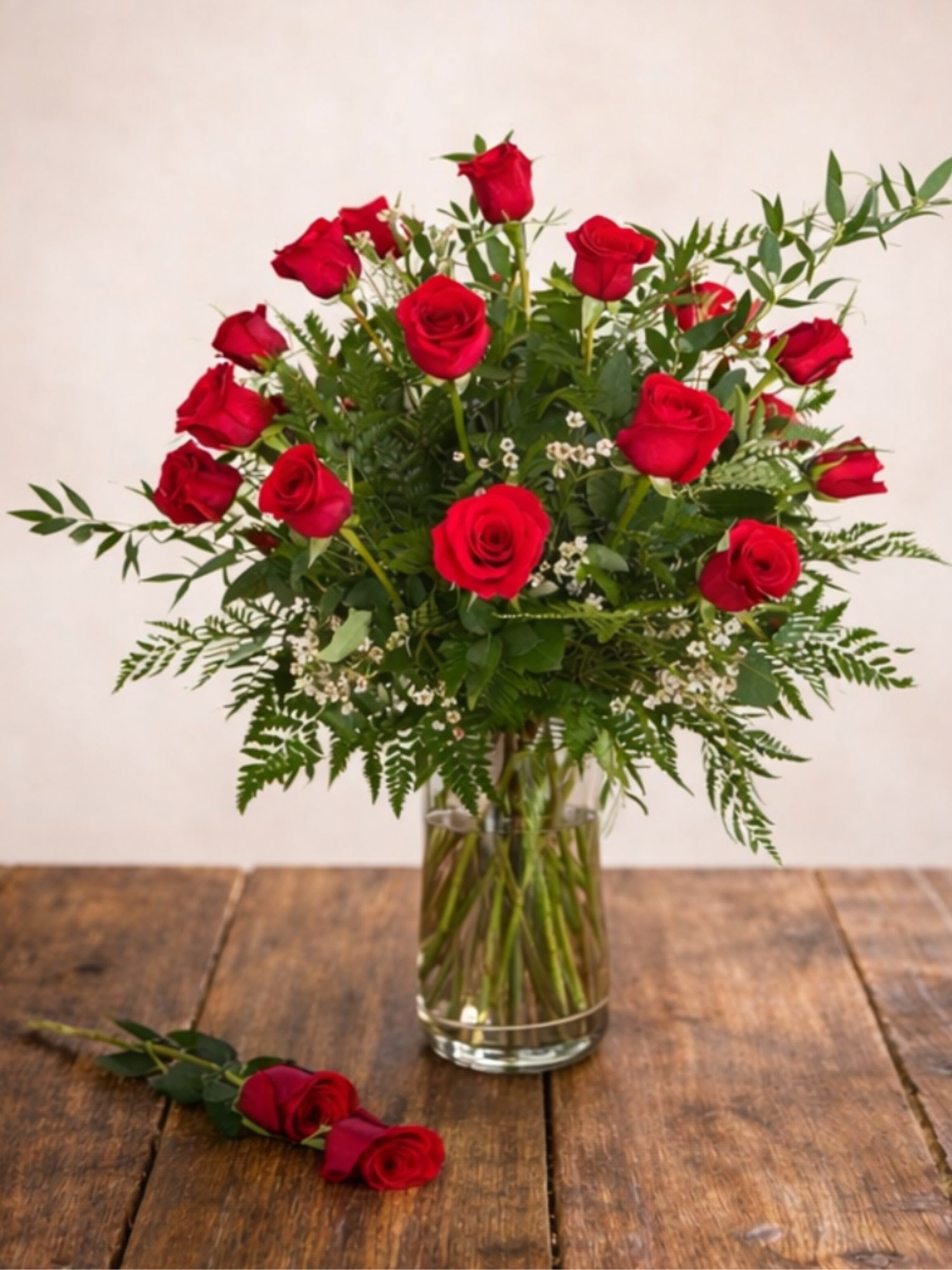 Red roses arranged in a clear glass vase with a matching rose on the table