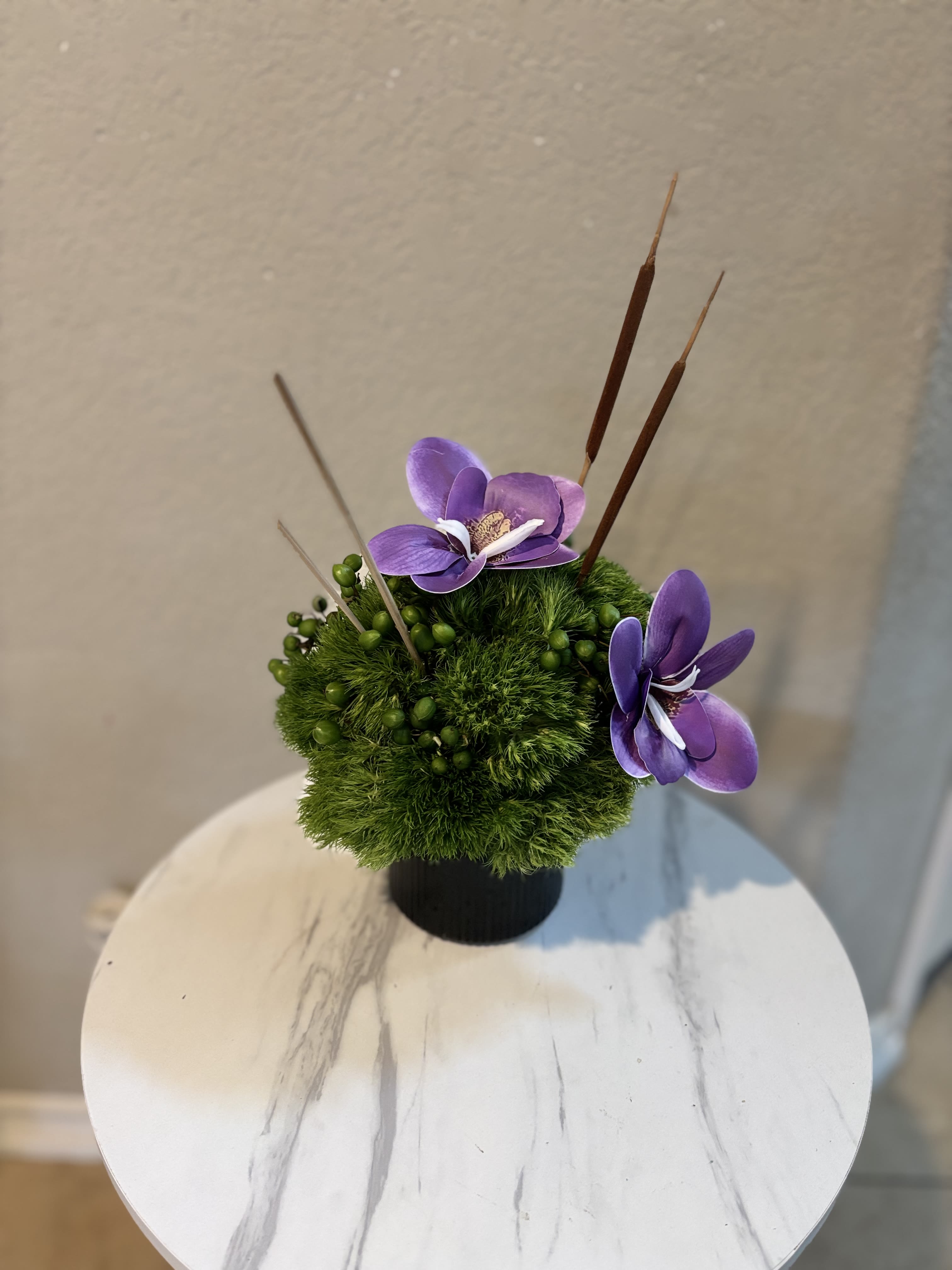 Small green floral arrangement with purple orchid blooms in a black pot