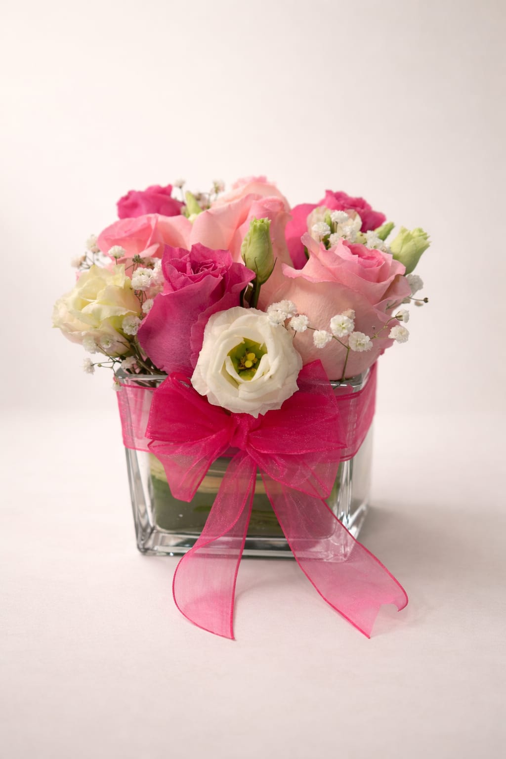 Pink and white roses arranged in a clear glass vase with a bright pink bow