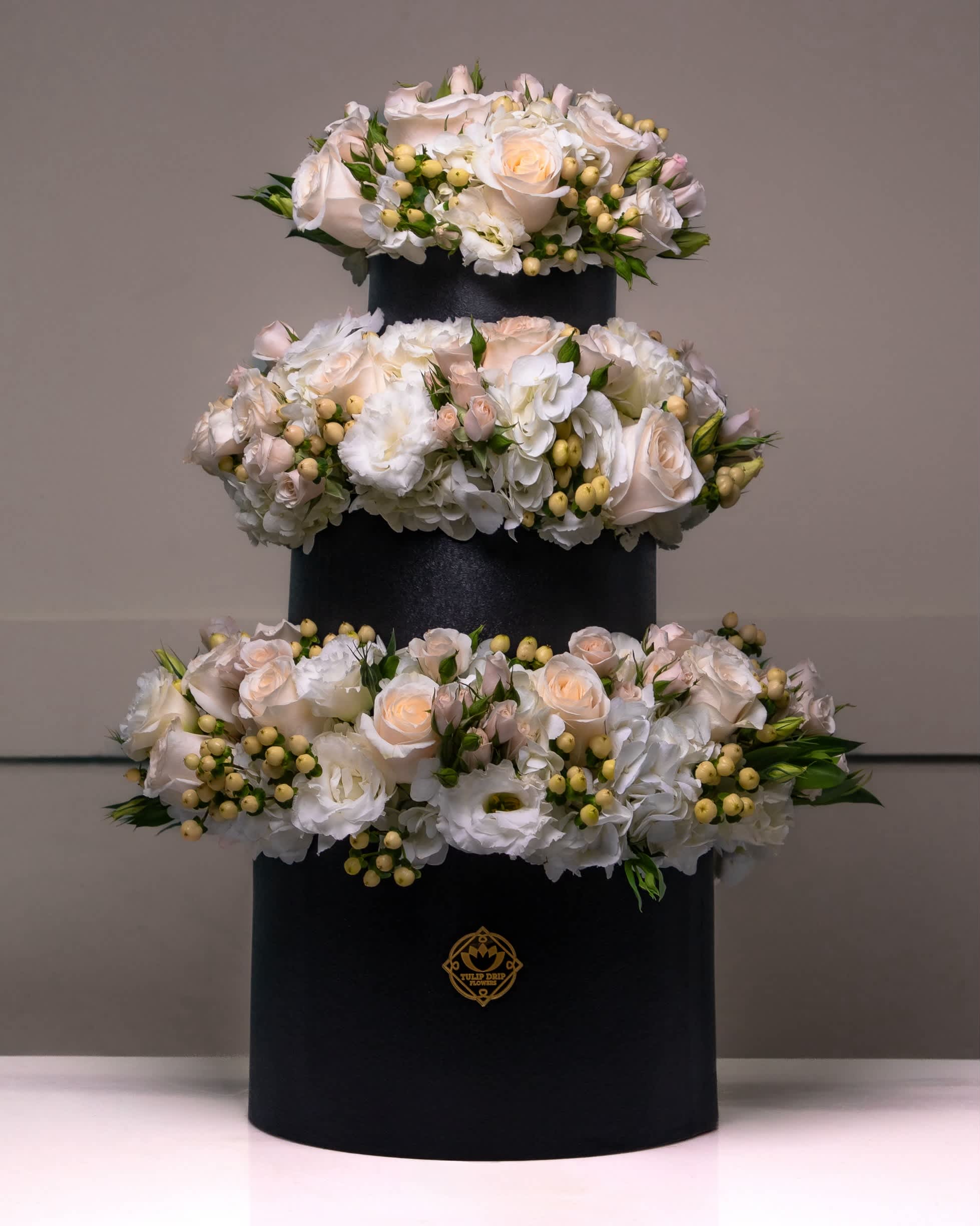 Three-tier floral arrangement of white and blush roses in a black box