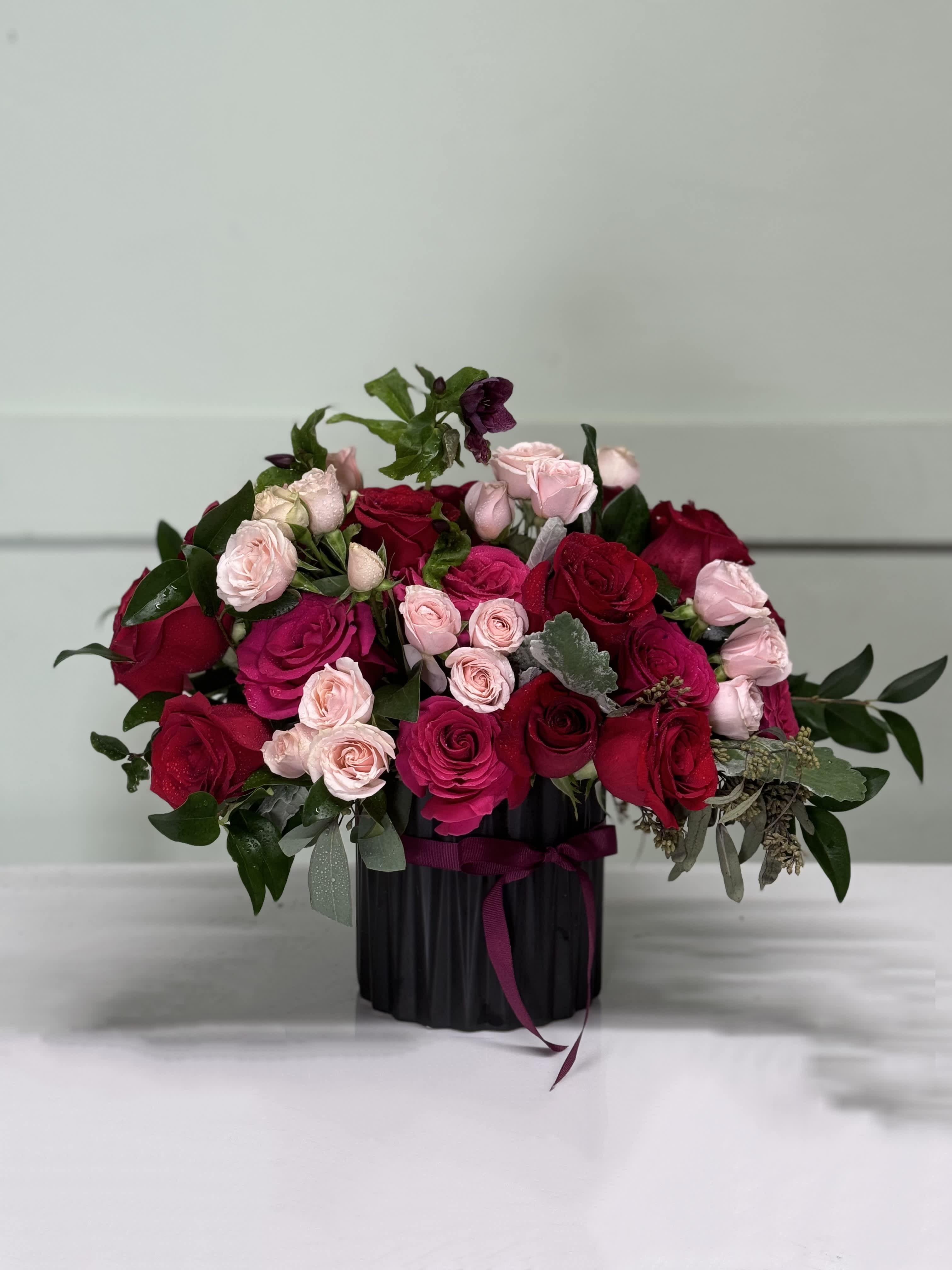 Bouquet of red and pink roses in a black vase with ribbon