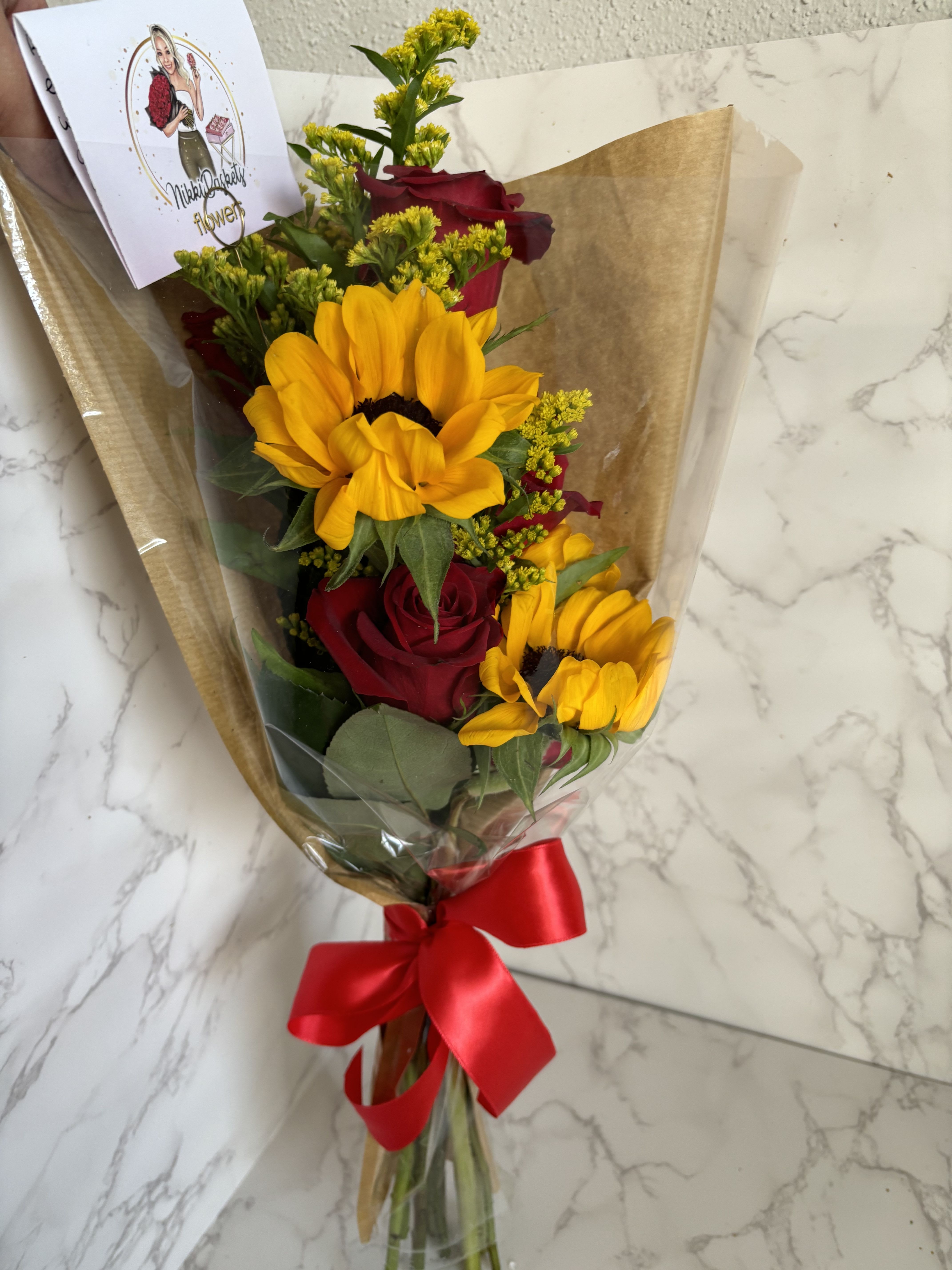 Bouquet of red roses and yellow sunflowers wrapped in brown paper with a red ribbon