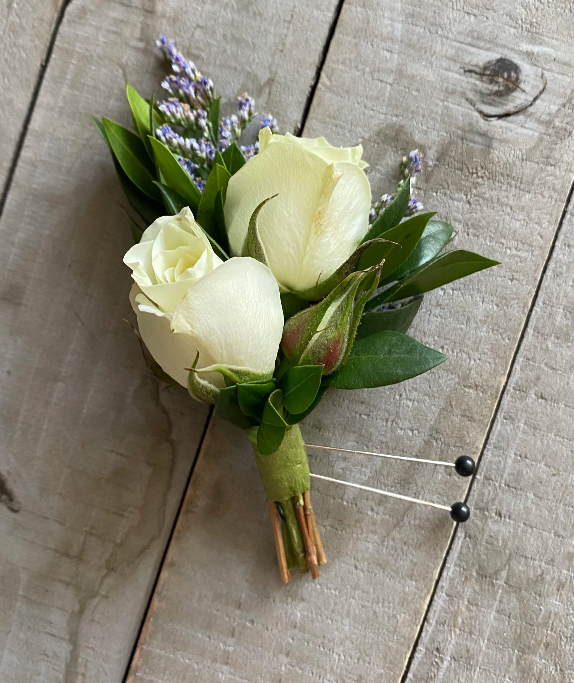 White rose boutonniere with purple filler flowers and green leaves