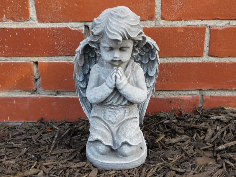 Small praying angel statue in front of a brick wall
