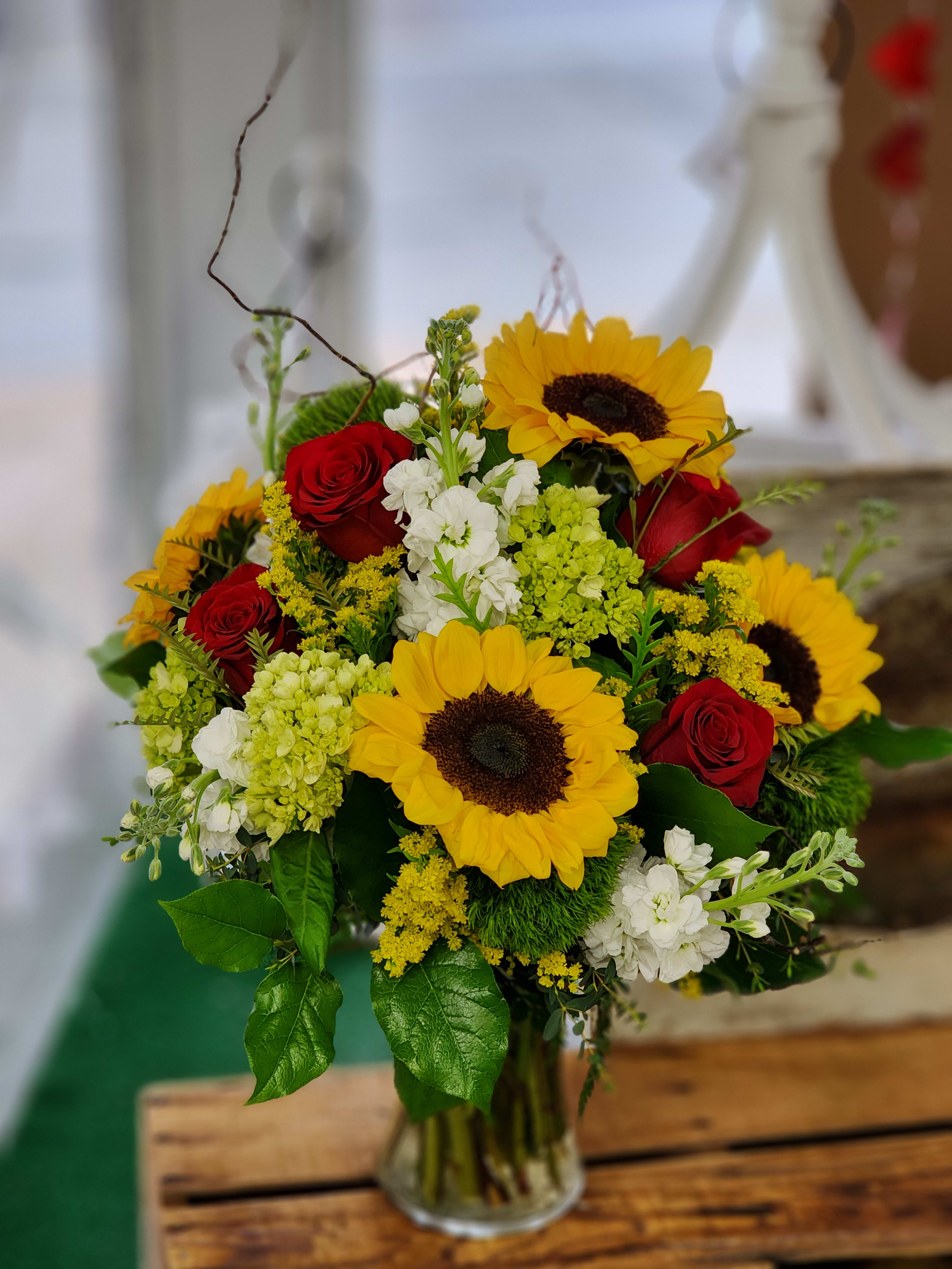 Bouquet of red roses and yellow sunflowers in a glass vase