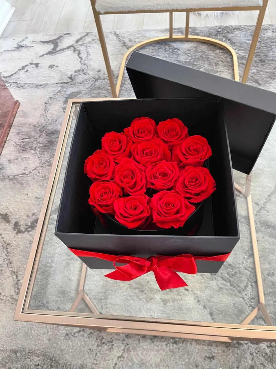 Forever Love - A striking cluster of vivid red roses arranged in a black hat box makes a bold statement for an anniversary, love-and-romance moment, or a "just because" surprise. The dramatic red-and-black color palette reads instantly romantic and refined, so the person you're thinking of will feel deeply seen the moment the lid is lifted.  Each arrangement features tightly packed red roses-petals lush and velvety-set in a polished black round or square box. A bright red satin ribbon wraps the box and finishes in a large bow at the front, creating a compact, luxurious presentation that's both formal and intimate. The low, dense design keeps blooms secure and showcases the color contrast for maximum visual impact.  Perfect for saying "thank you," marking a milestone anniversary, or adding romance to Valentine's Day, this arrangement arrives ready to gift and makes a memorable centerpiece on a bedside table or dining room. Boxes are designed for easy display; remove the bow for a more understated look and refresh water per standard rose care to extend bloom life.