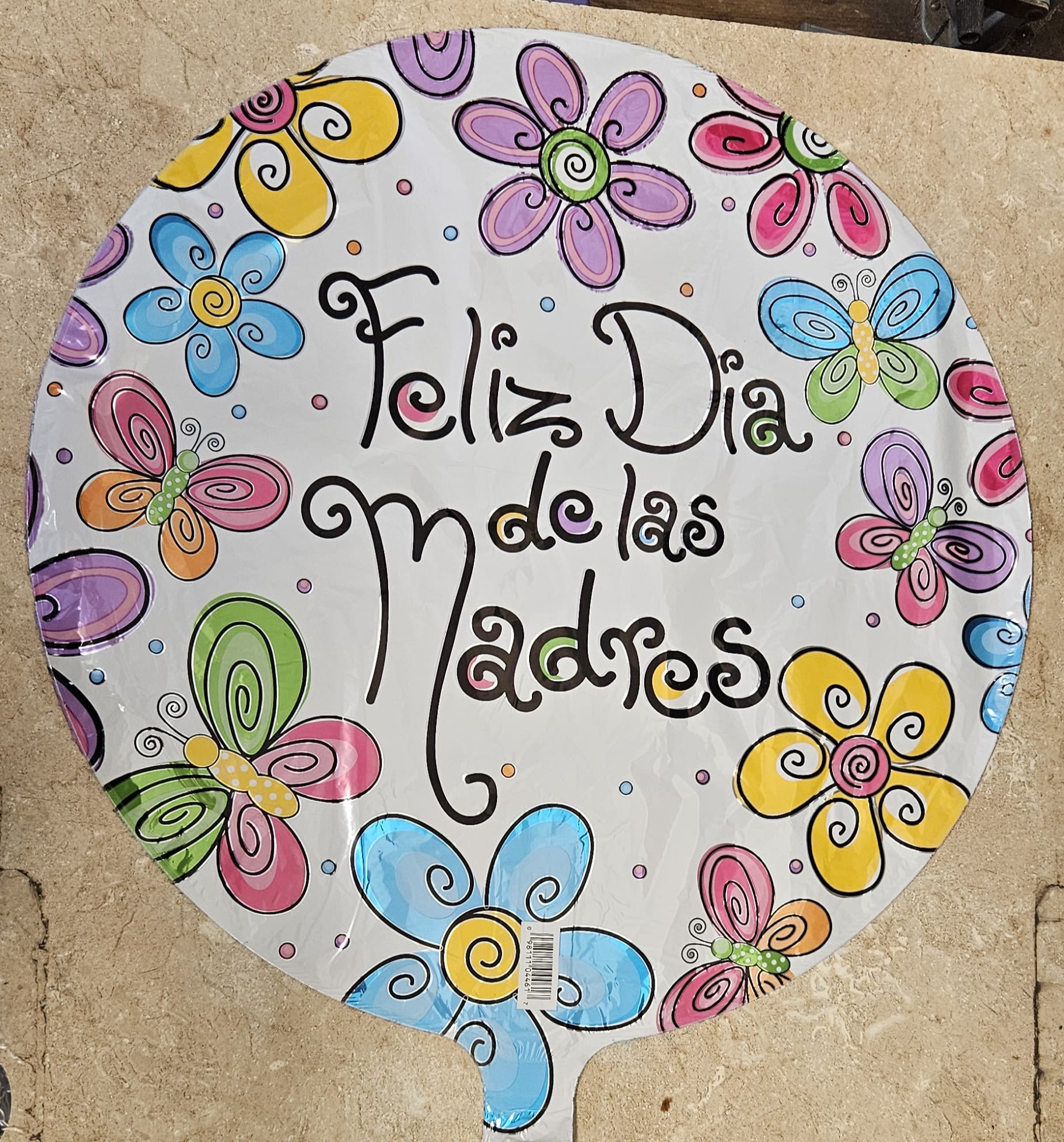 Feliz Dia de las Madres - Bright, cheerful and unmistakably celebratory-this Mother's Day arrangement pairs a festive round foil balloon printed with "Feliz Dia de las Madres" and a playful mix of cartoon-style flowers and butterflies in pink, blue, yellow, purple, and green. Perfect as a Mother's Day gift or to brighten a brunch table, this colorful balloon sends a joyful, heartfelt message that will make the mom you're thinking of feel loved and celebrated.  The design sits on a clean white background with flat, graphic blooms and fluttering butterflies for a fun, modern look that suits moms who appreciate whimsy and color. Because this product is a foil balloon rather than fresh flowers, it's an excellent add-on to gifts, cakes, or simple deliveries-no vase needed. Order options include standard sizing for single-burst display and secure inflation for delivery; for longevity, keep the balloon indoors away from sharp edges and extreme heat.