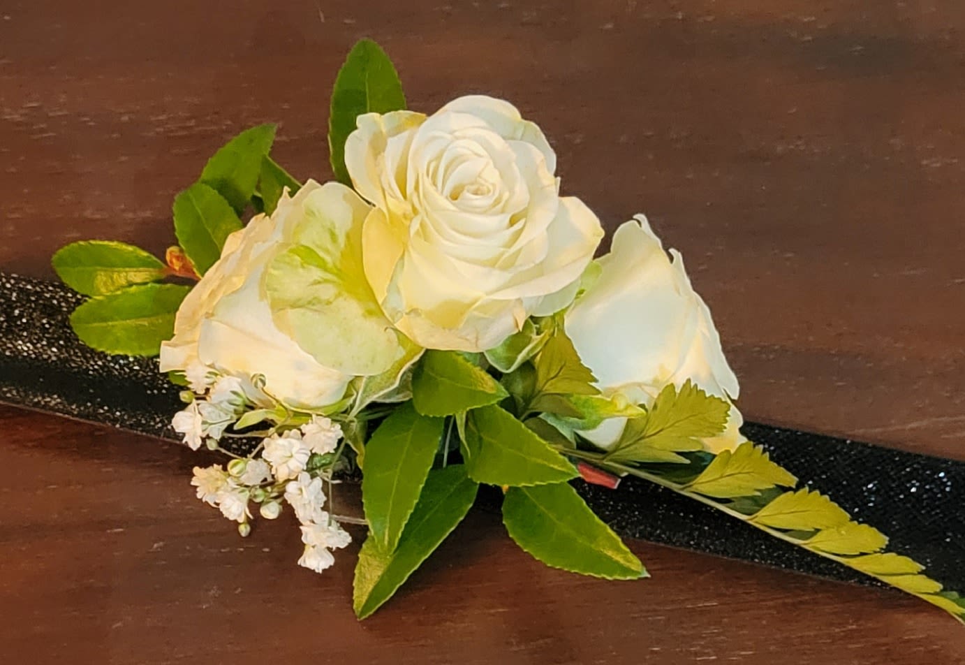 White rose boutonniere with green leaves and a black ribbon