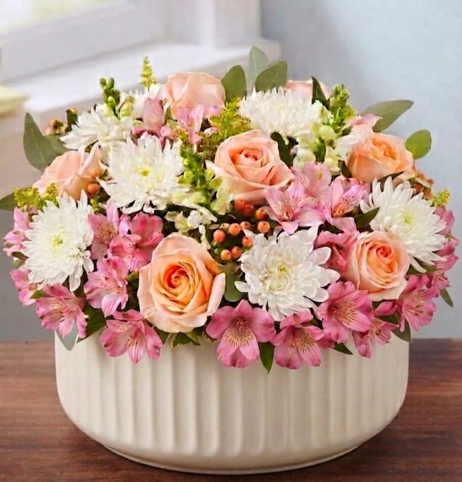 Penny Hatbox (Now in a ceramic container!) - EXCLUSIVE An exquisite gift with garden-inspired style. Our blush-colored gathering of blooms is arranged in our signature European hatbox: an elegant, new dove gray container finished with a matching ribbon. Its versatile design is perfect for displaying a variety of colors, adding a special touch to any occasion.  All-around arrangement with peach roses, white snapdragons and mums, pink Peruvian lilies (alstroemeria); accented with peach hypericum, silver dollar eucalyptus and assorted greenery