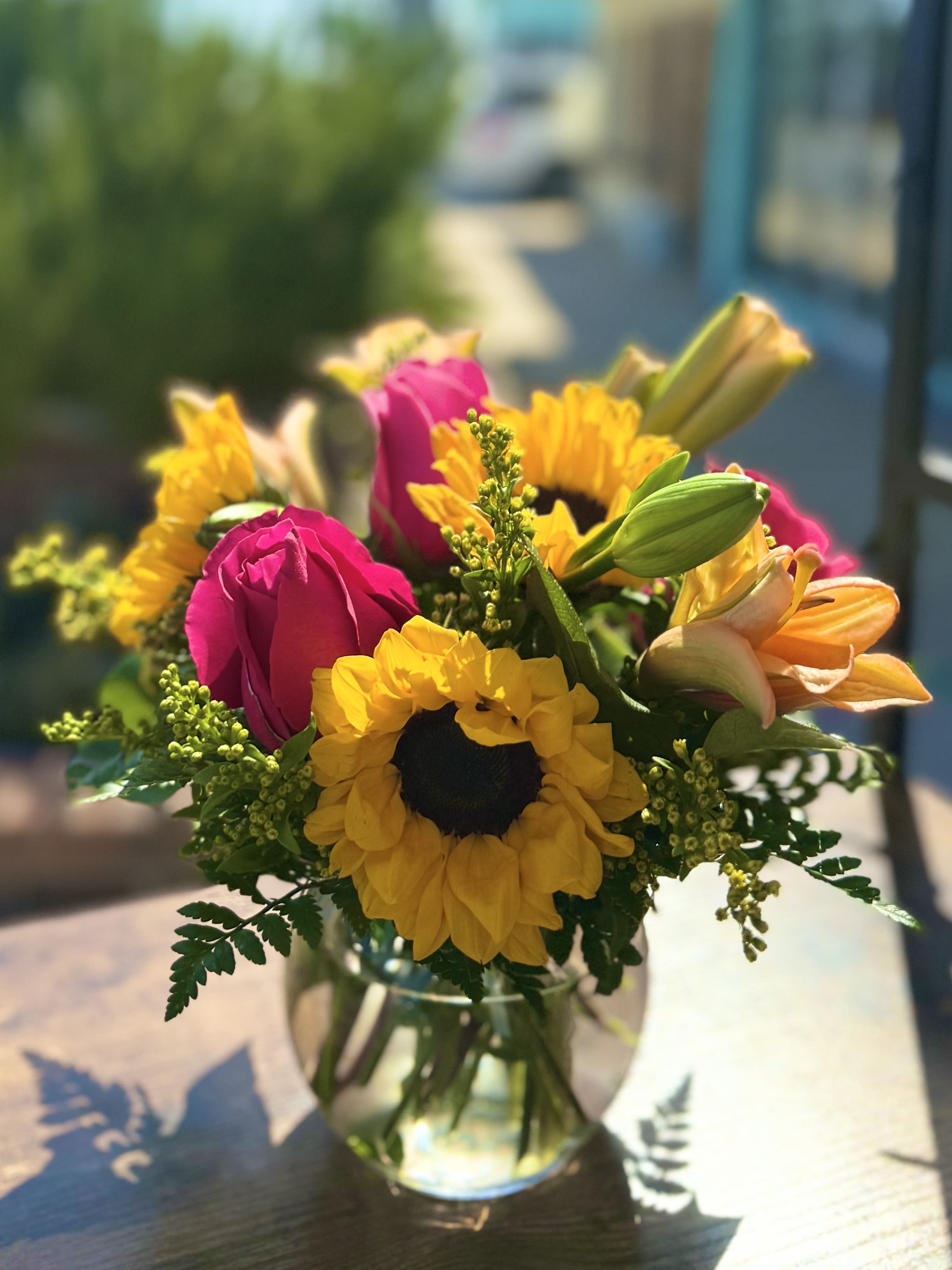 Bouquet of pink roses, yellow sunflowers, and orange lilies in a glass vase