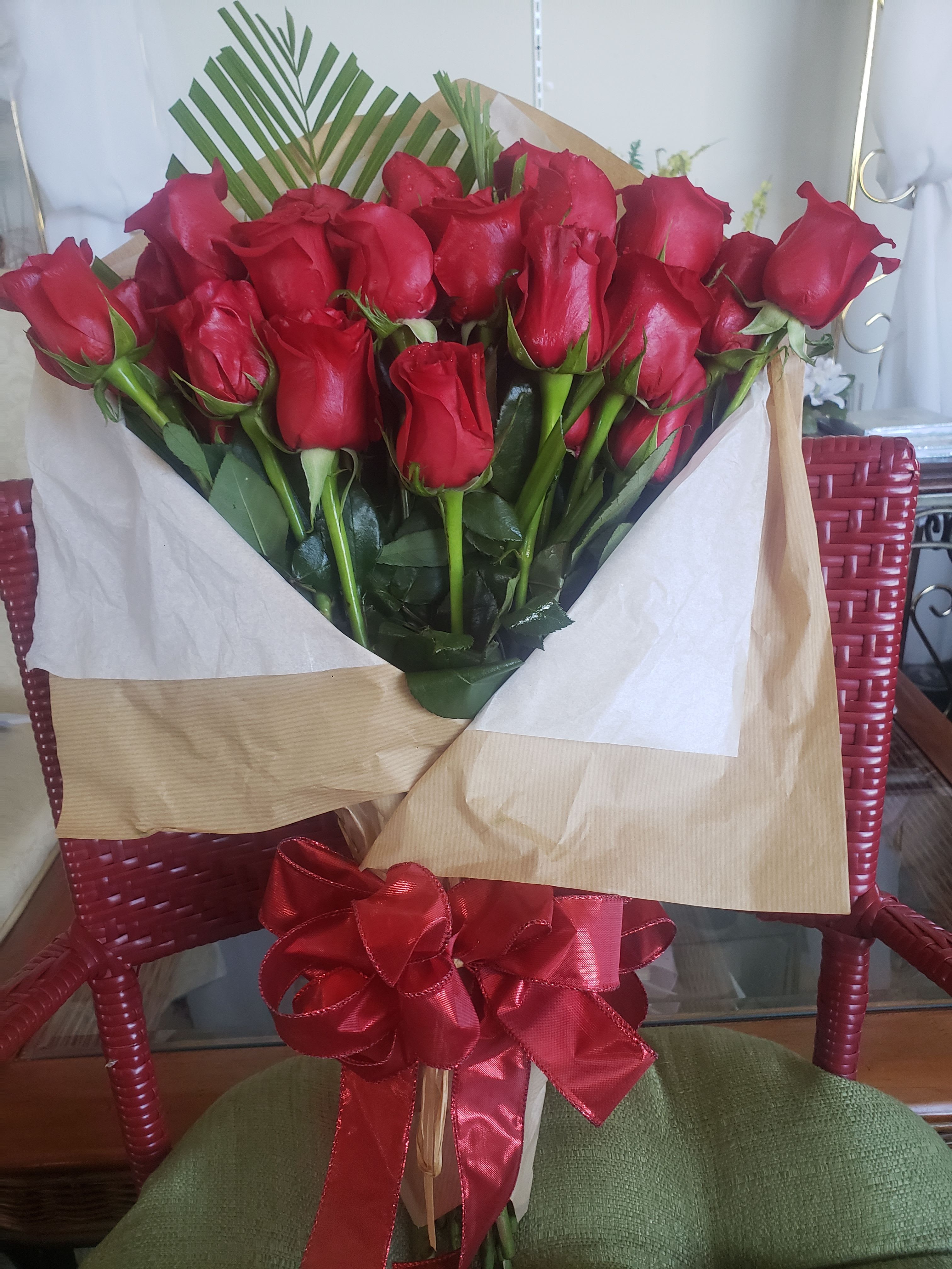 WISHING WRAP BOUQUET - A dense cluster of velvety red roses gathered into a hand-tied bouquet creates an immediate romantic statement - perfect as a Valentine's Day bouquet or an anniversary roses gift. The red-on-neutral contrast gives the blooms dramatic presence so the person you're sending it to will feel truly seen and celebrated the moment the paper is unfolded.  Wrapped in layered tan (brown kraft) and white paper with white tissue accents and finished with a large red satin ribbon, this wishing-wrap bouquet reads as classic and polished - the kind of arrangement that looks equally elegant in hand or on a bedside table. The tight, full heads of red roses provide rich color and texture; the neutral paper keeps the focus on the blooms while the glossy red bow gives a gift-ready final flourish.  Ideal for saying "I love you," celebrating an anniversary, or making a romantic surprise, this bouquet comes ready to present and makes an immediate impression. For best enjoyment, keep the stems in fresh water and away from direct heat or sunlight to preserve bloom life.