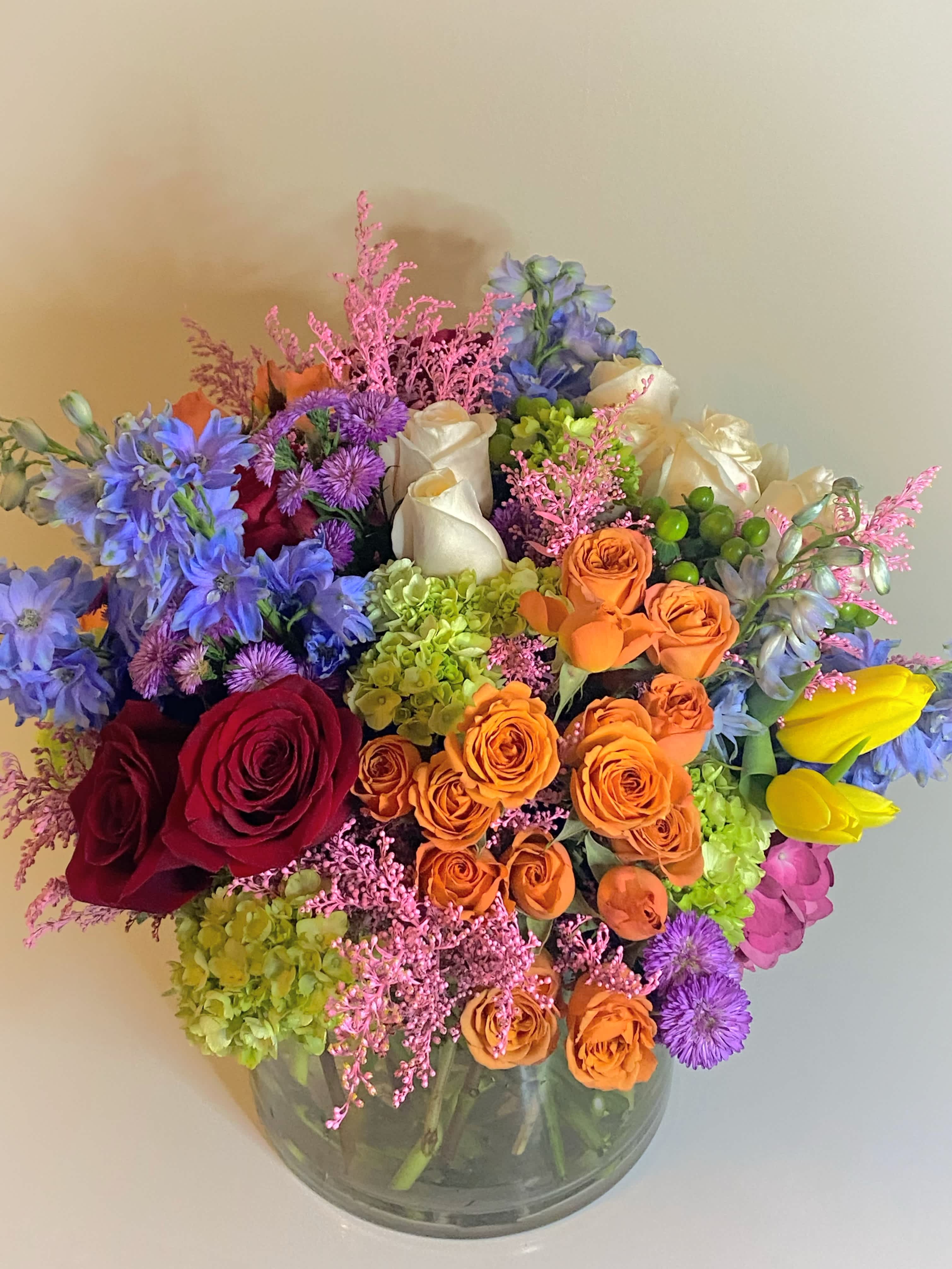 Mixed bouquet of roses, hydrangeas, and blue flowers in a glass vase