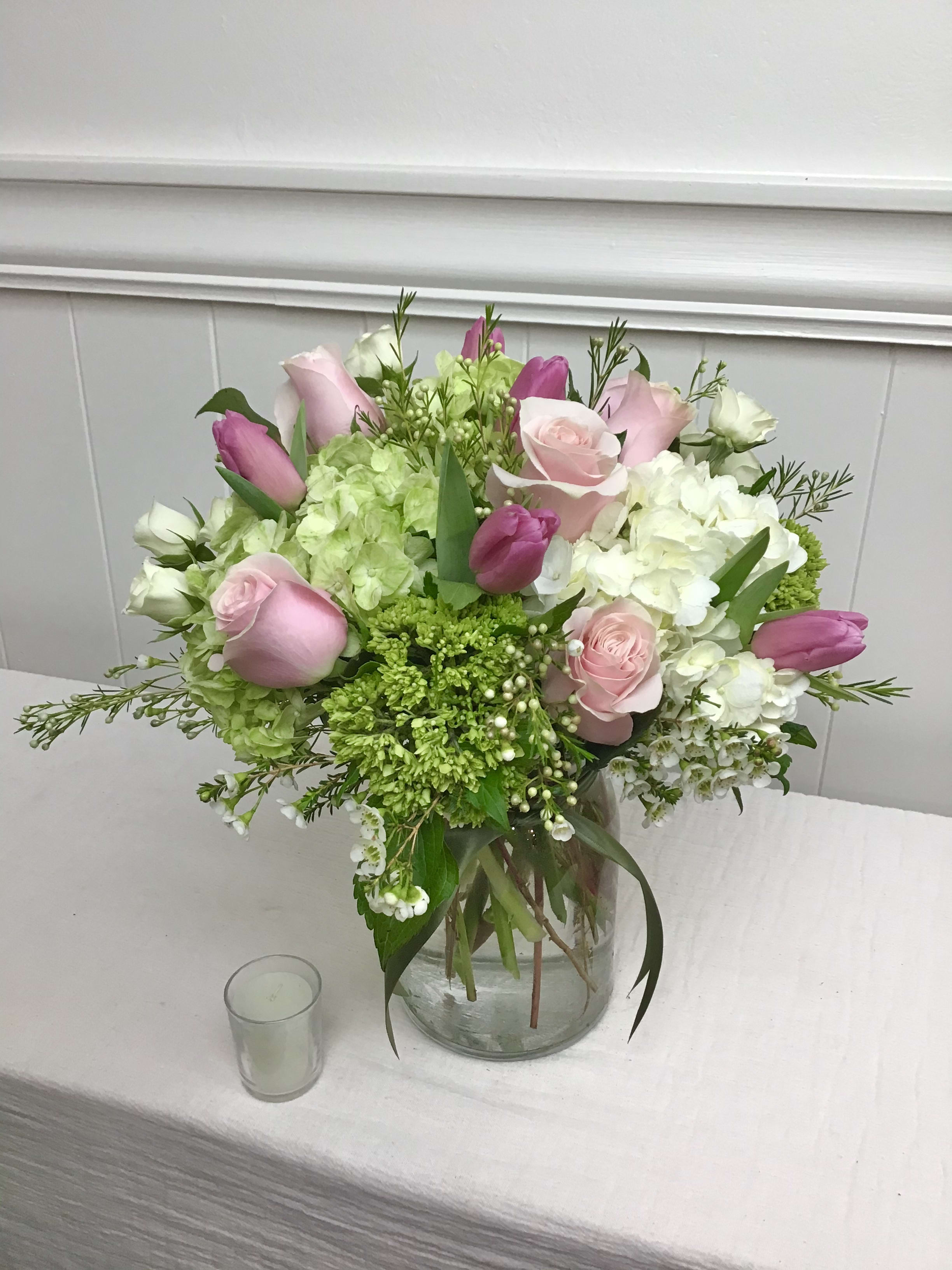 Pink roses and tulips with white hydrangeas in a clear glass vase on a table