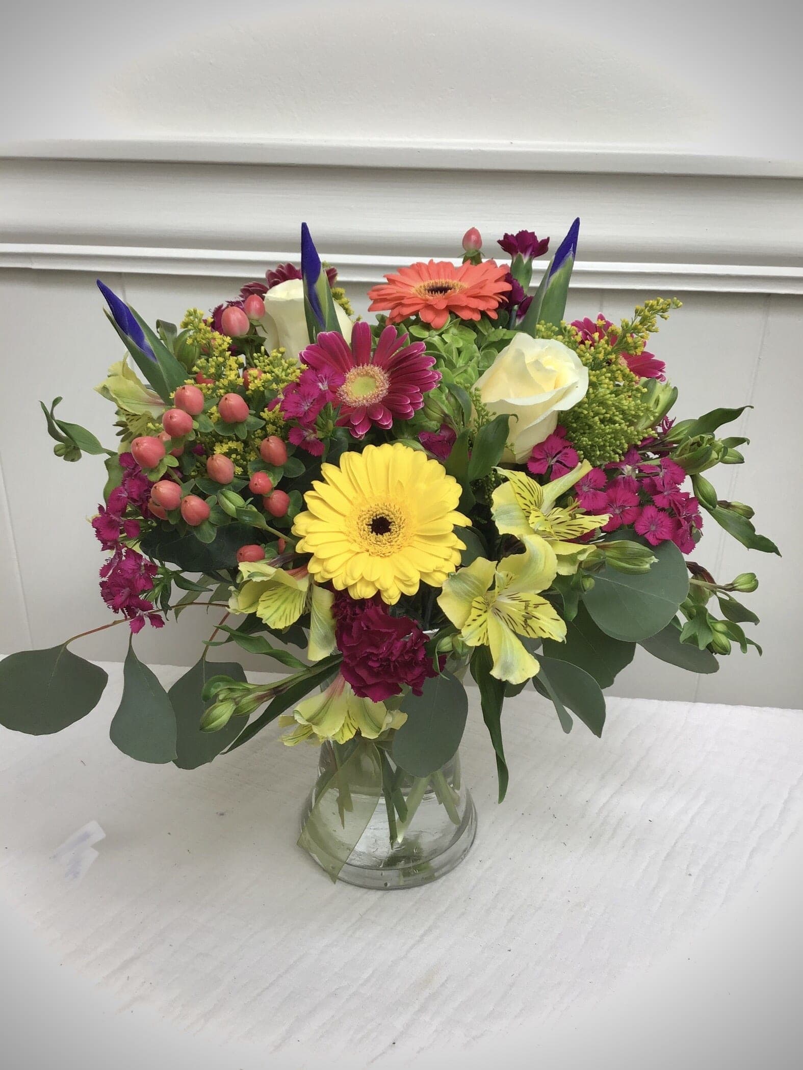Bright mixed bouquet of gerbera daisies, roses, and other blooms in a clear glass vase