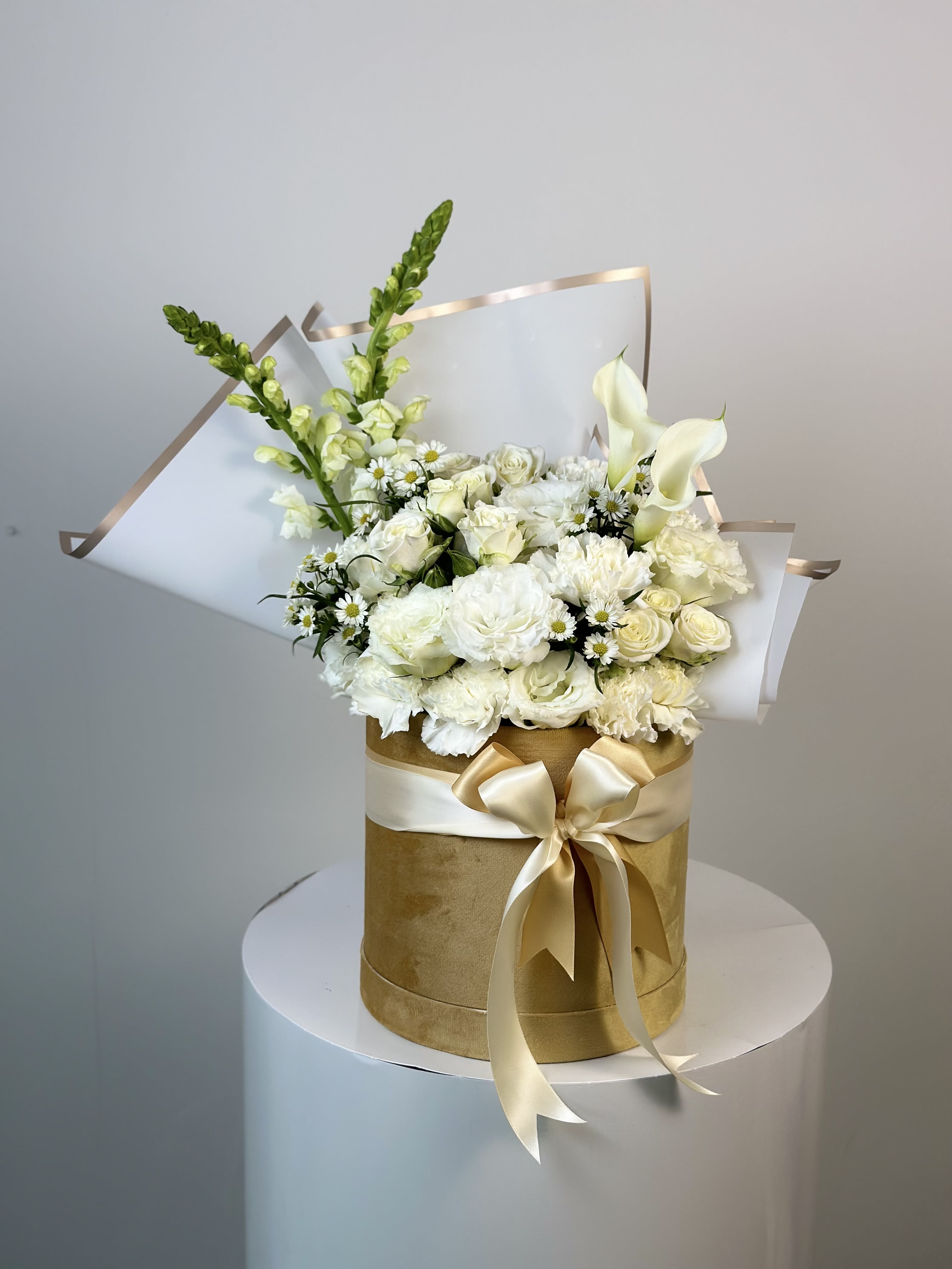 White floral bouquet in a gold hatbox with a satin bow