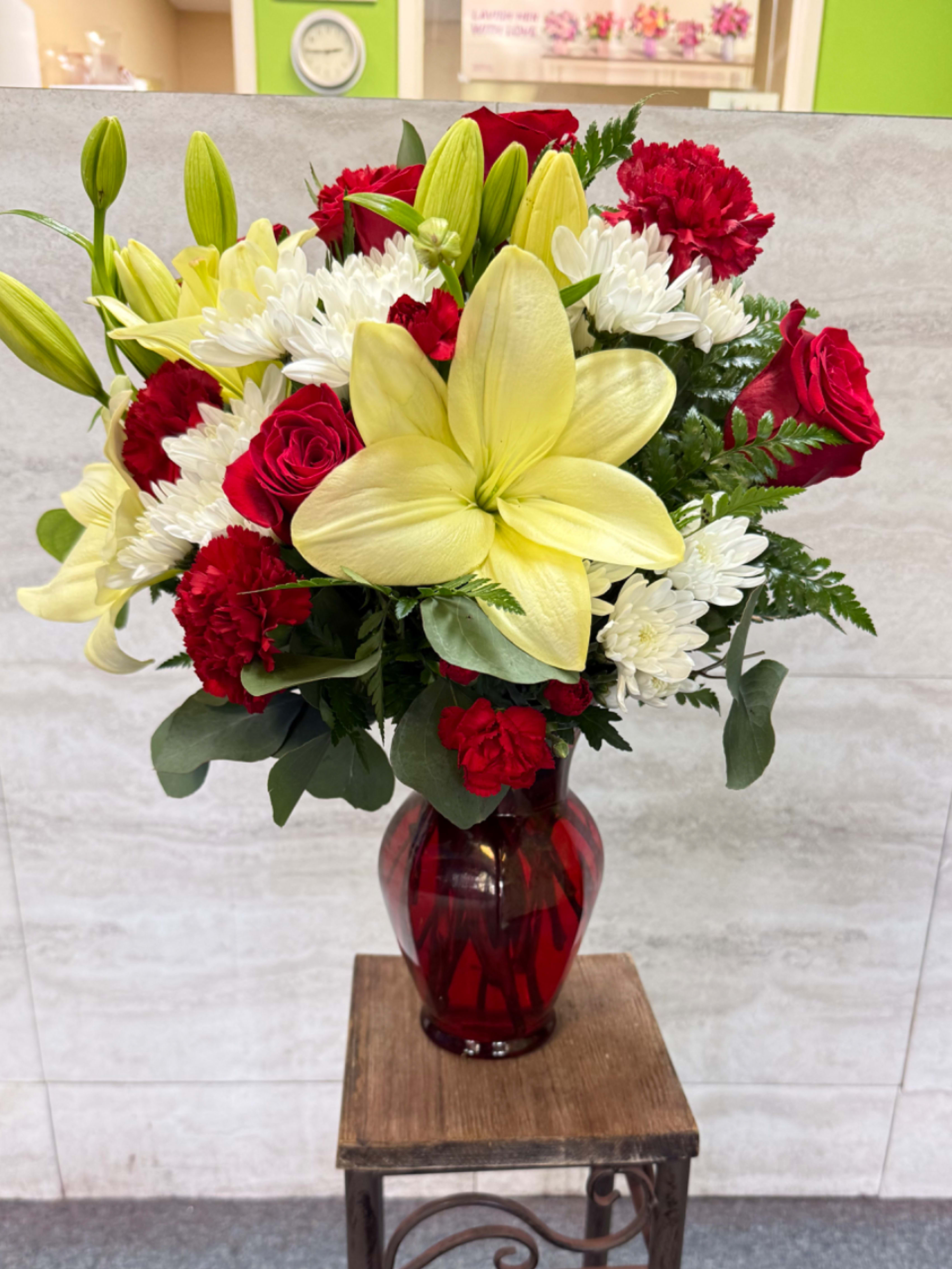 Bouquet of red roses, white chrysanthemums, and yellow lilies in a red glass vase
