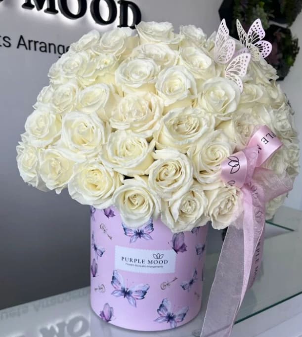 50 White Roses With Butterflies In a Box - Container size D8.25'x H9.5'  White roses in a butterfly box. Delicate and enchanting, our 50 White Roses with Butterflies arrangement is designed to capture hearts. Pure white roses are beautifully arranged in a pastel butterfly-themed hatbox, symbolizing grace, purity, and transformation. Adorned with decorative butterflies and finished with a satin ribbon, this bouquet is perfect for elegant celebrations, thoughtful gestures, or creating a lasting impression of beauty and serenity. Perfect for a baby girl.   •    50 premium white roses arranged in a luxury butterfly-print hatbox     •    Embellished with delicate butterfly accents and satin ribbon     •    Represents purity, elegance, and new beginnings   