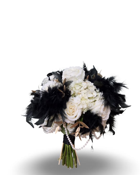 Roaring Romance Prom Posy - A couture-ready hand-tied posy that reads like eveningwear: white roses and clustered white hydrangea form the soft, luminous core of this event bouquet, while dramatic black feathers and draped pearl strands give it a bold, fashion-forward edge - perfect for a wedding, gala, or prom where the recipient should feel truly seen.  Tightly gathered with visible stems and finished with decorative ribbon and pearl accents, the compact Roaring Romance Posy mixes classic blooms and theatrical textures for high-contrast impact. The monochrome palette with sculptural black feathers and subtle pearl details creates a formal, embellished look that pairs beautifully with evening dress or bridal attire.  Sized as a handheld arrangement, this posy is designed for presentation moments. Bouquet comes in a vase with minimal water to keep bouquet fresh. 