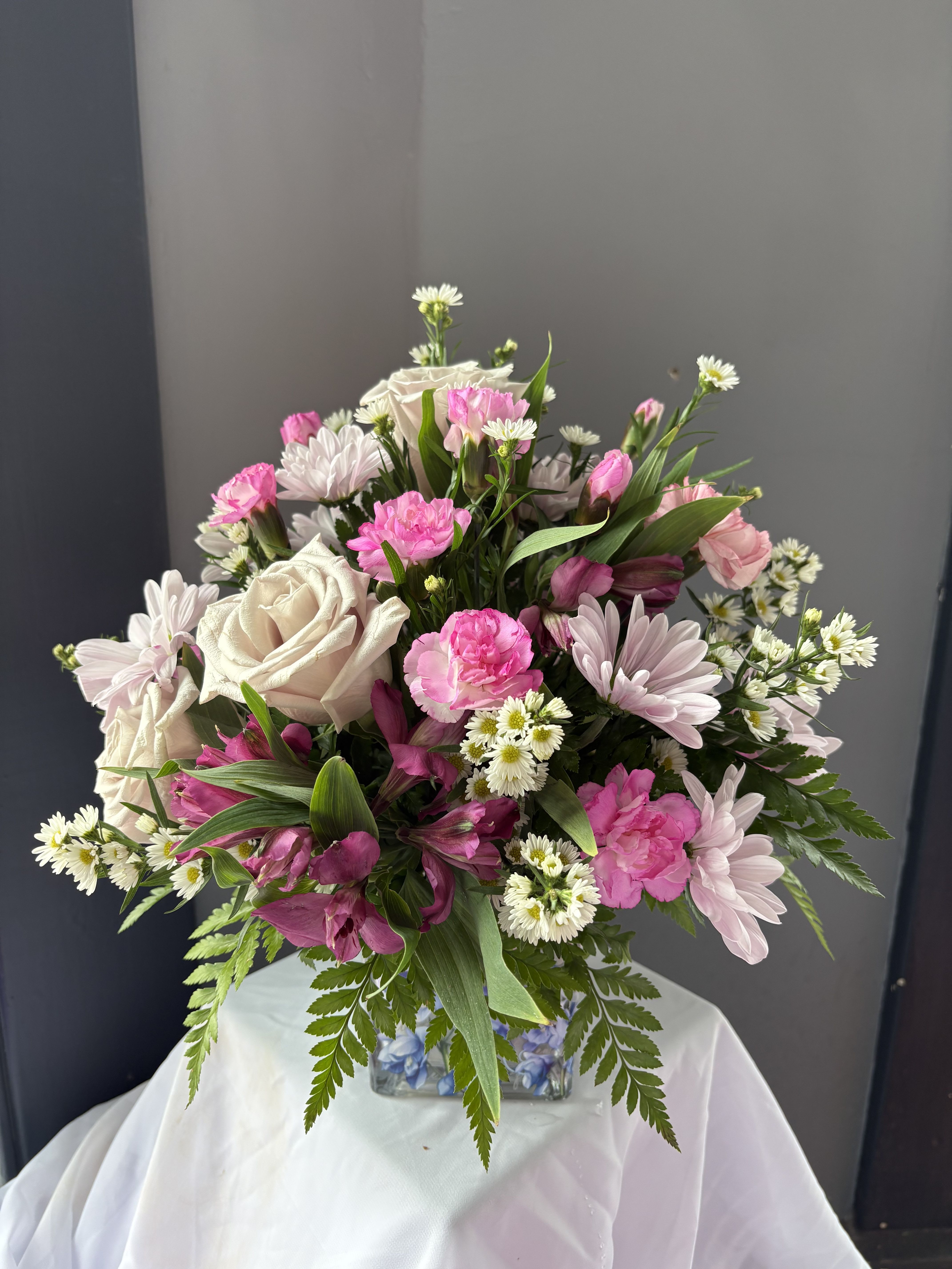 Frazier's Flowers Written In The Sky Bouquet - Peaceful and poetic, Frazier's Version Written In The Sky Bouquet inspires serenity with lavender roses, lavender daisies, pink mini carnations, purple alstroemeria, and white monte arranged in a glass cube adorned with delicate flowers and a graceful dove design.