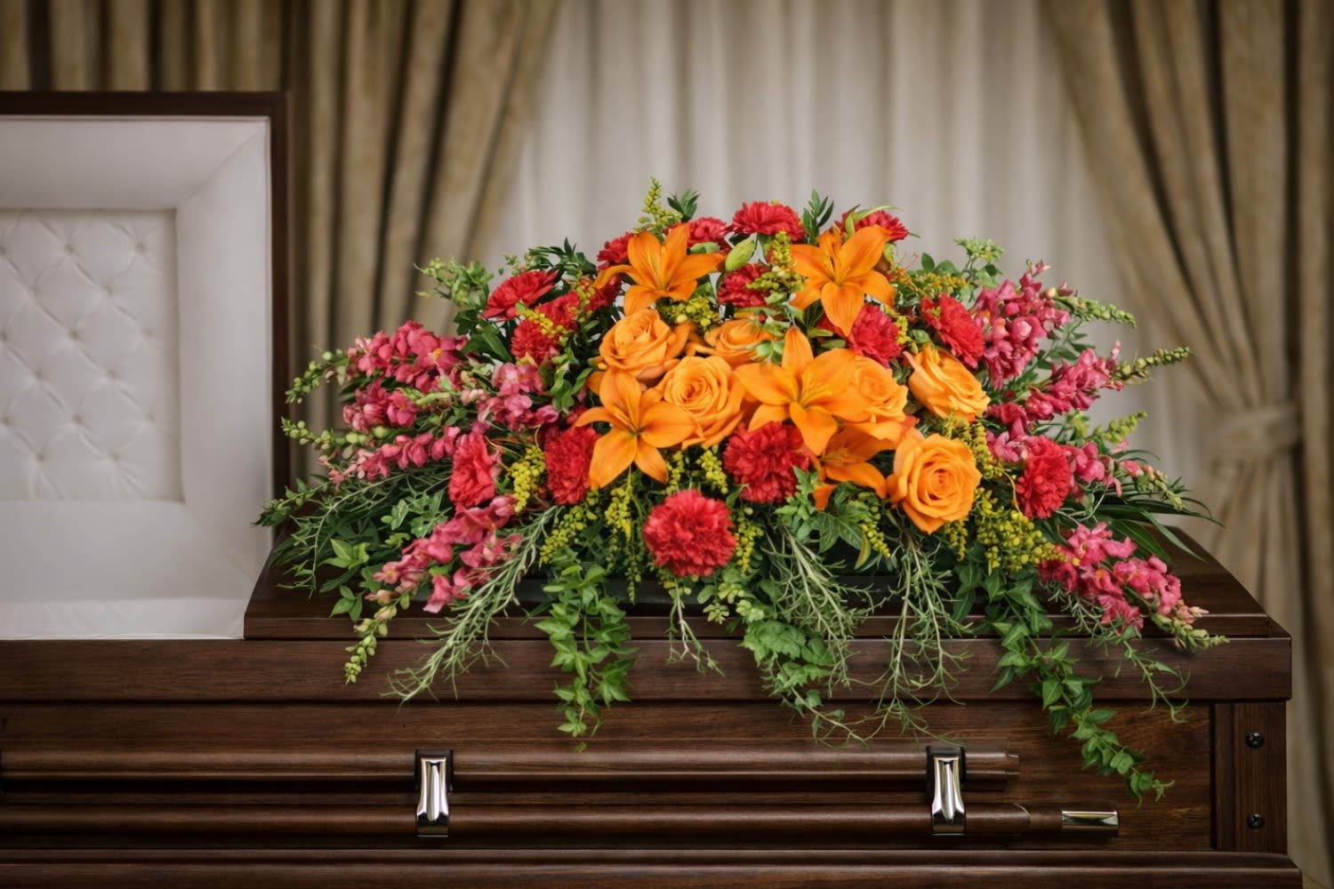 Tribute Casket Spray  - The Tribute Casket Spray from FloralFabulous is a vibrant and heartfelt expression of love, remembrance, and honor. This beautifully designed funeral arrangement features radiant orange roses, striking orange lilies, rich red carnations, and delicate snapdragons, all accented with lush flowing greenery.  The warm tones of orange and red symbolize love, strength, admiration, and deep respect, making this arrangement a meaningful tribute to celebrate a life well lived. Designed to rest gracefully atop the casket, the Tribute Casket Spray creates a stunning focal point during funeral and memorial services, offering comfort and support to family and friends.  Its cascading greenery and full floral design provide movement and elegance, reflecting both the beauty of cherished memories and the lasting impact of a loved one’s life.  FloralFabulous proudly provides funeral flower delivery and casket sprays in Round Rock, TX and the greater Austin area, helping families express love, remembrance, and heartfelt support during life’s most difficult moments