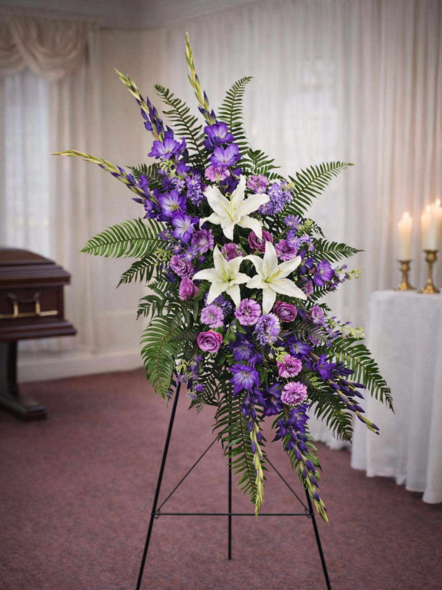 Lavender Memories Sympathy Standing Spray - The Lavender Memories Standing Spray from FloralFabulous is a beautiful and heartfelt sympathy tribute designed to honor a life remembered with love. This elegant standing arrangement features graceful white lilies surrounded by soft lavender and purple blooms including gladiolus, lisianthus, stock, and asters.  Accented with lush ferns and fresh greenery, the flowing design creates a peaceful and comforting presence during funeral services and memorial gatherings. The calming lavender and purple tones symbolize dignity, remembrance, and admiration, making this arrangement a meaningful expression of sympathy for family and friends.  Designed as a traditional standing spray, the Lavender Memories arrangement creates a striking display beside the casket or memorial setting, offering comfort while celebrating cherished memories of a loved one.  FloralFabulous proudly provides sympathy flower delivery for funeral services and memorial arrangements in Round Rock, TX and the greater Austin area, helping families express love, remembrance, and heartfelt support during times of loss.