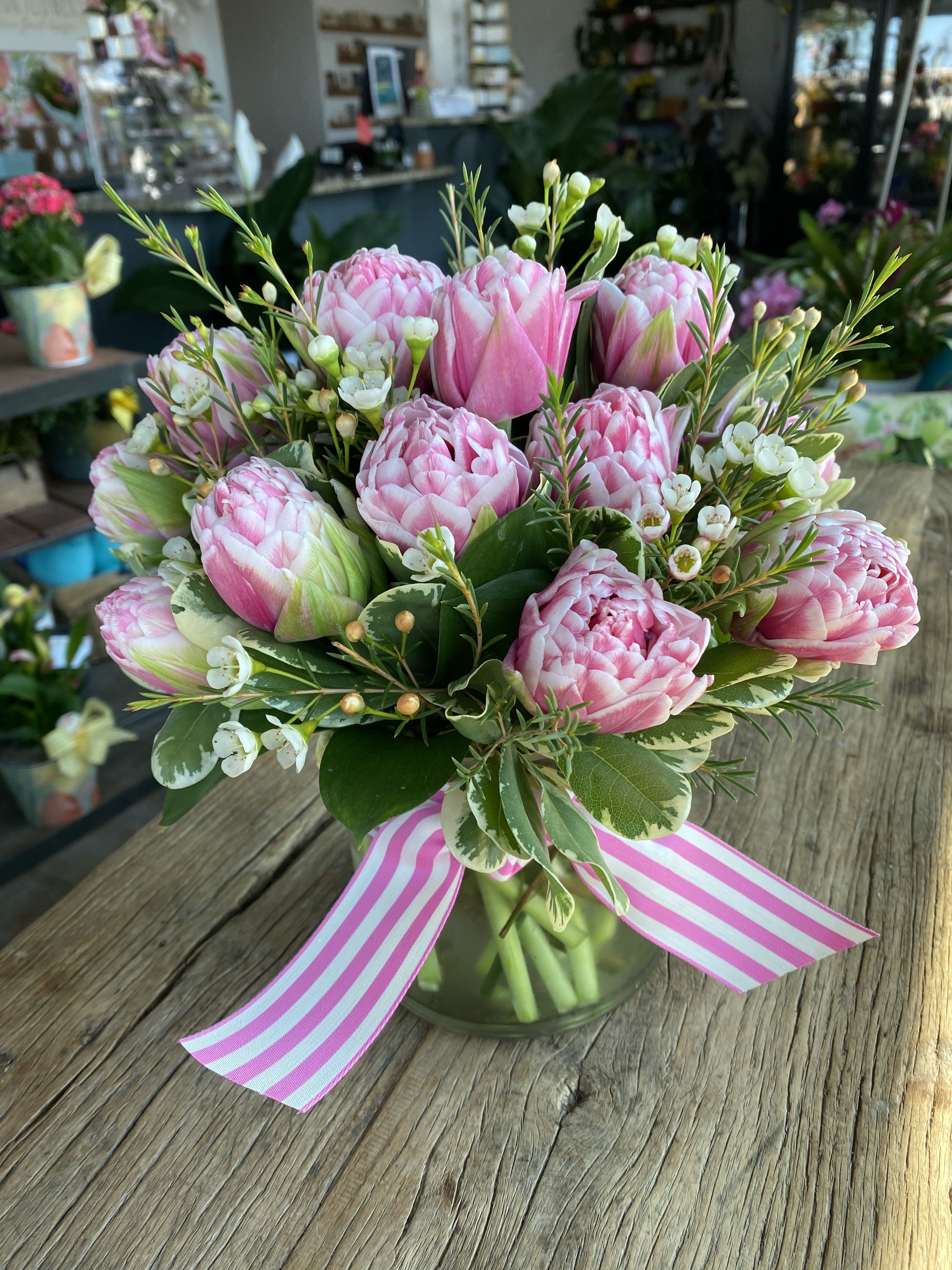 Pink tulip bouquet in a glass vase with a striped ribbon