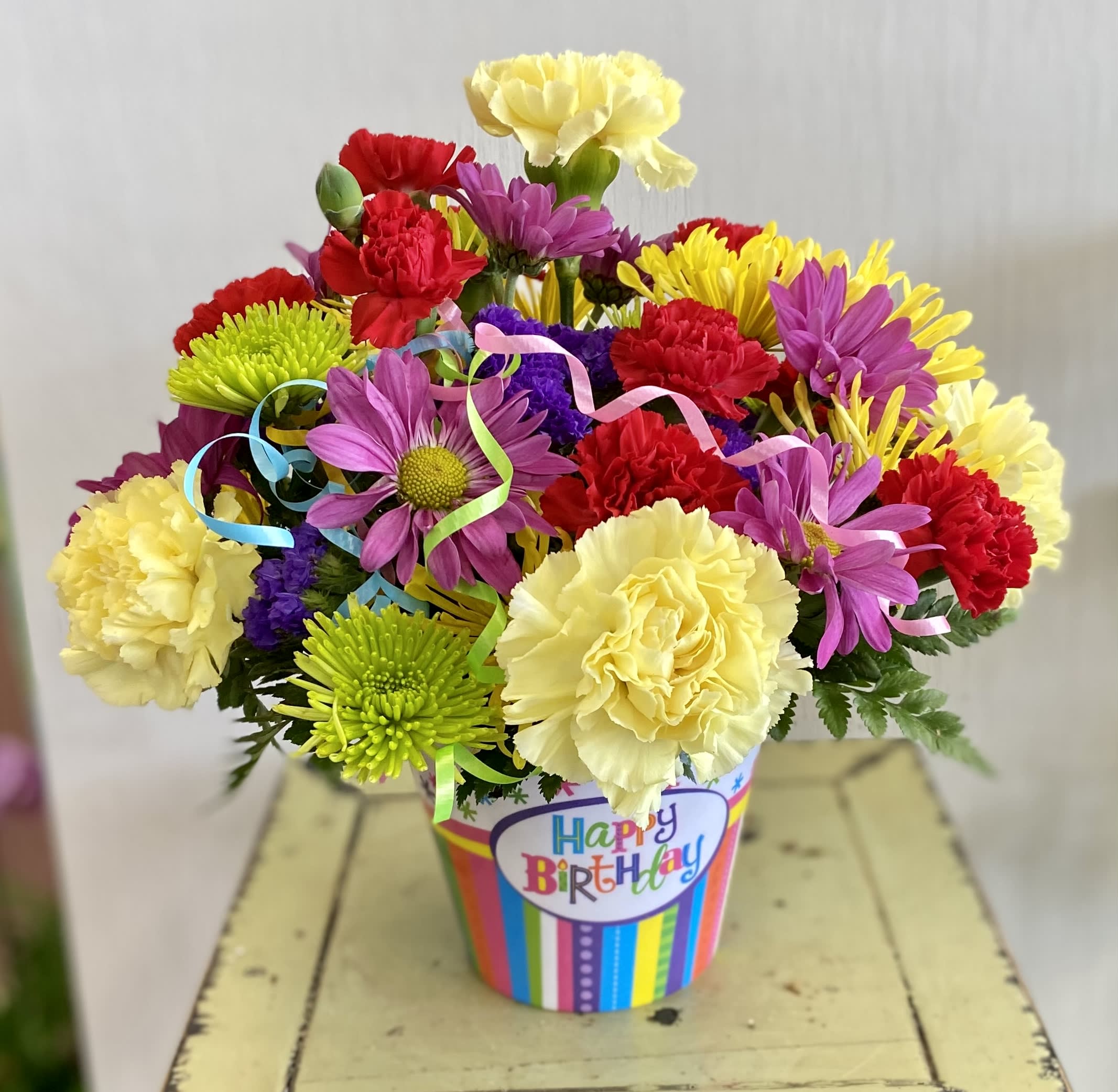 Colorful bouquet of carnations and daisies in a birthday container