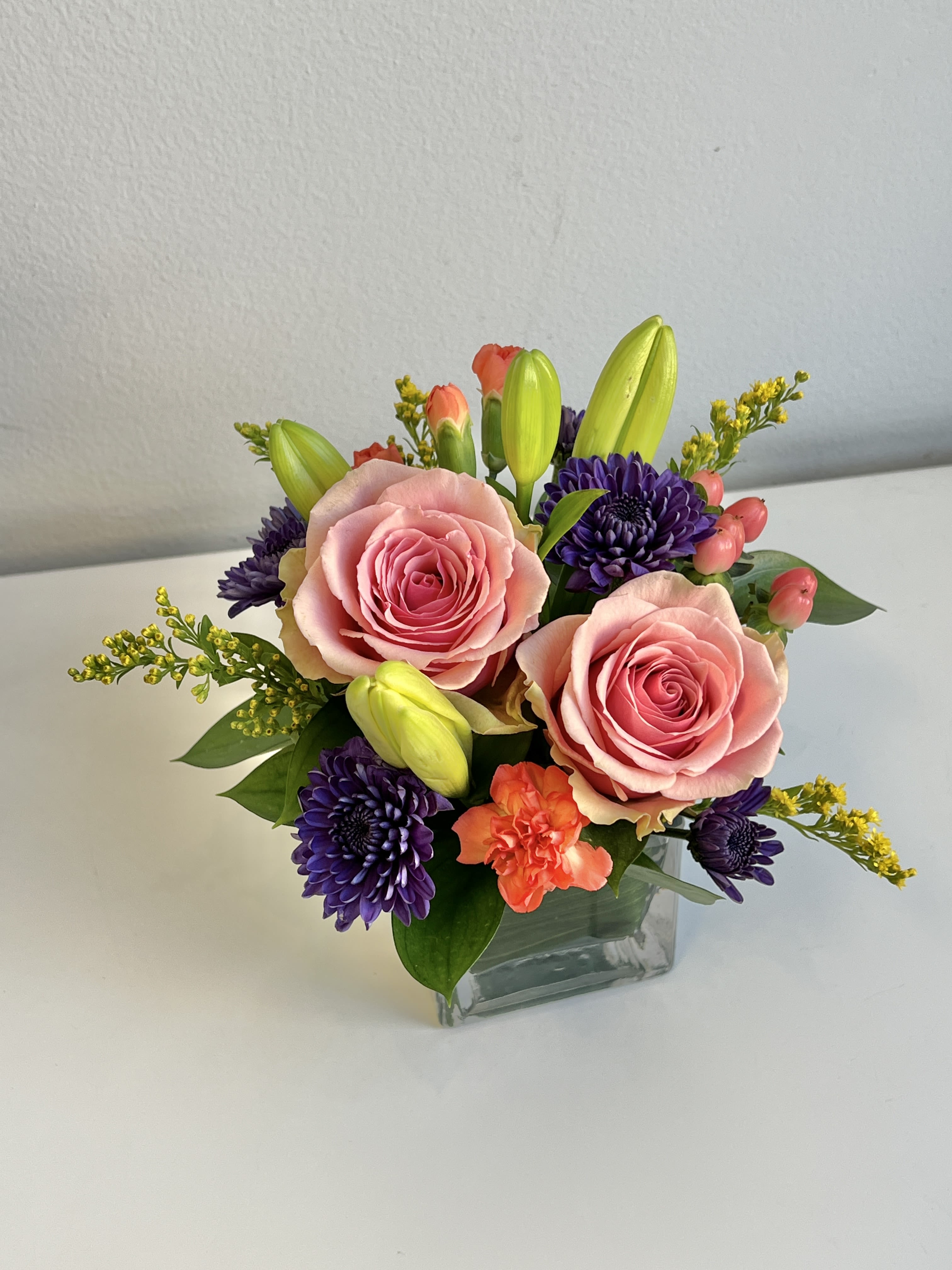 REG-15 - Yellow Lilies, Pink Roses, Bright Colored Pixies, Mums, Hypericum Berries, Yellow Solidego and Assorted Foliage in Small Glass Vase.