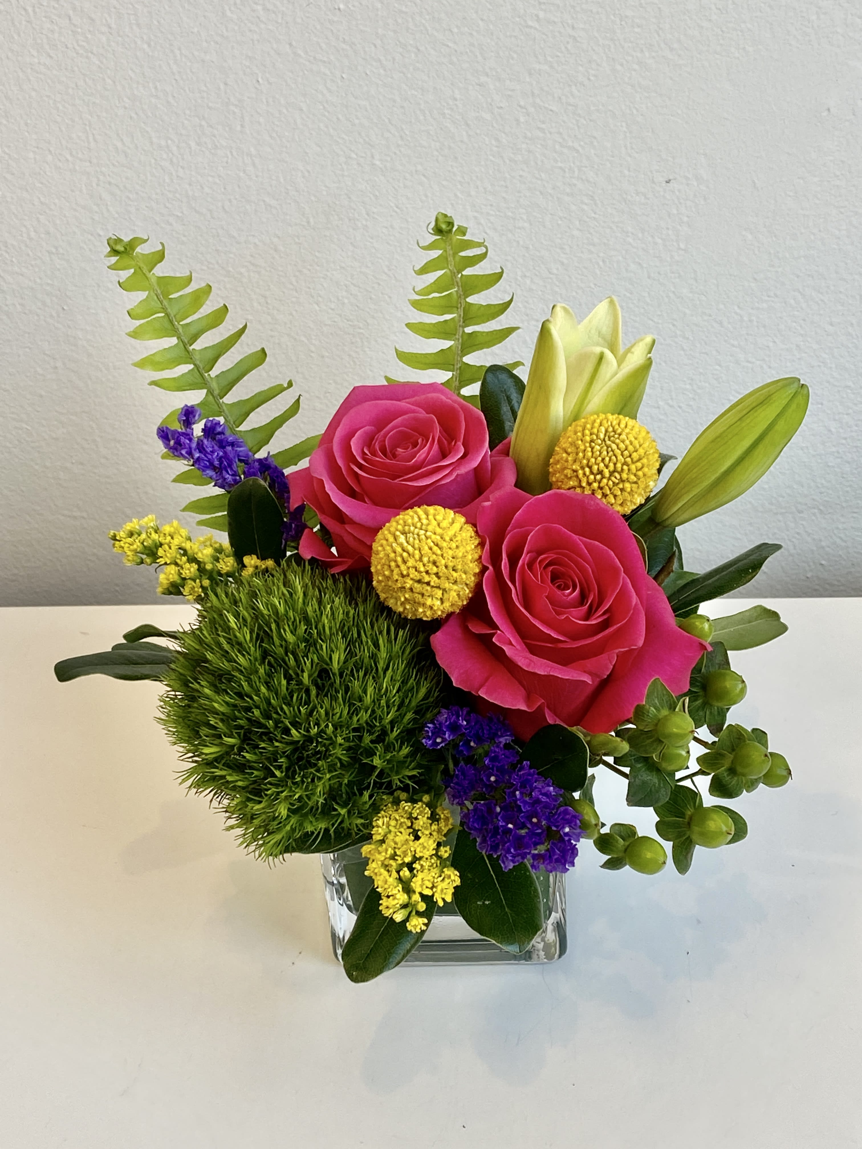 Pink roses in a clear square vase with yellow and purple accents