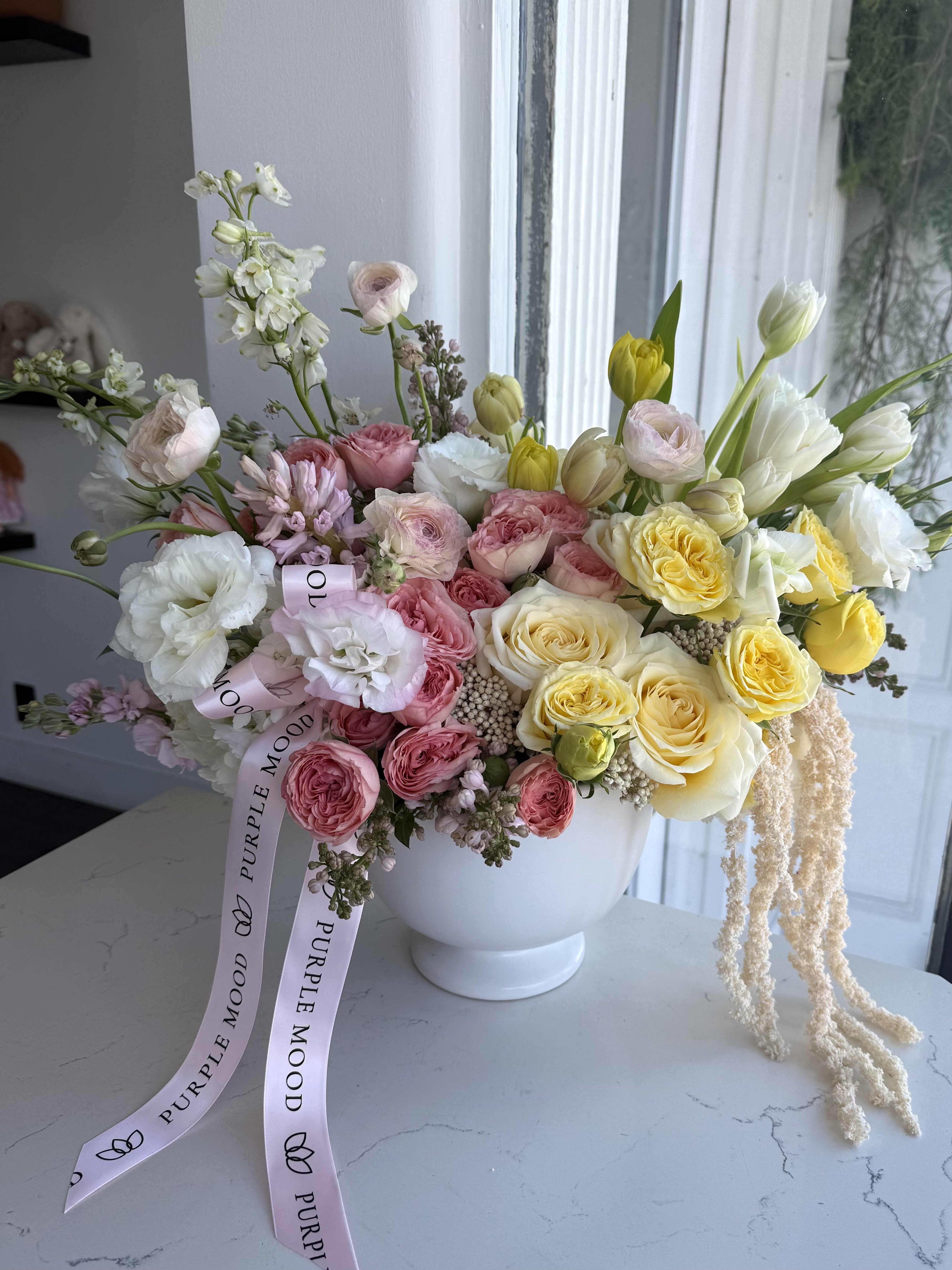 Creamy Lemon Vase - A delicate floral arrangement in a ceramic vase, filled with soft cream, blush pink, and sunny yellow tones that bring warmth and light into any space. Lush roses, elegant ranunculus, and seasonal blooms create an airy, romantic feel, while flowing accents add a graceful, modern touch. Finished with a soft ribbon for an extra hint of charm. A perfect gift that speaks of love, care, and effortless beauty