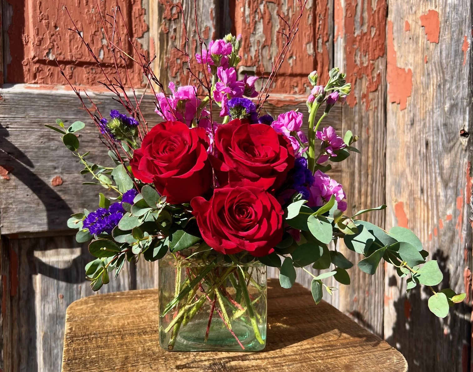 Red roses and purple flowers in a clear glass vase