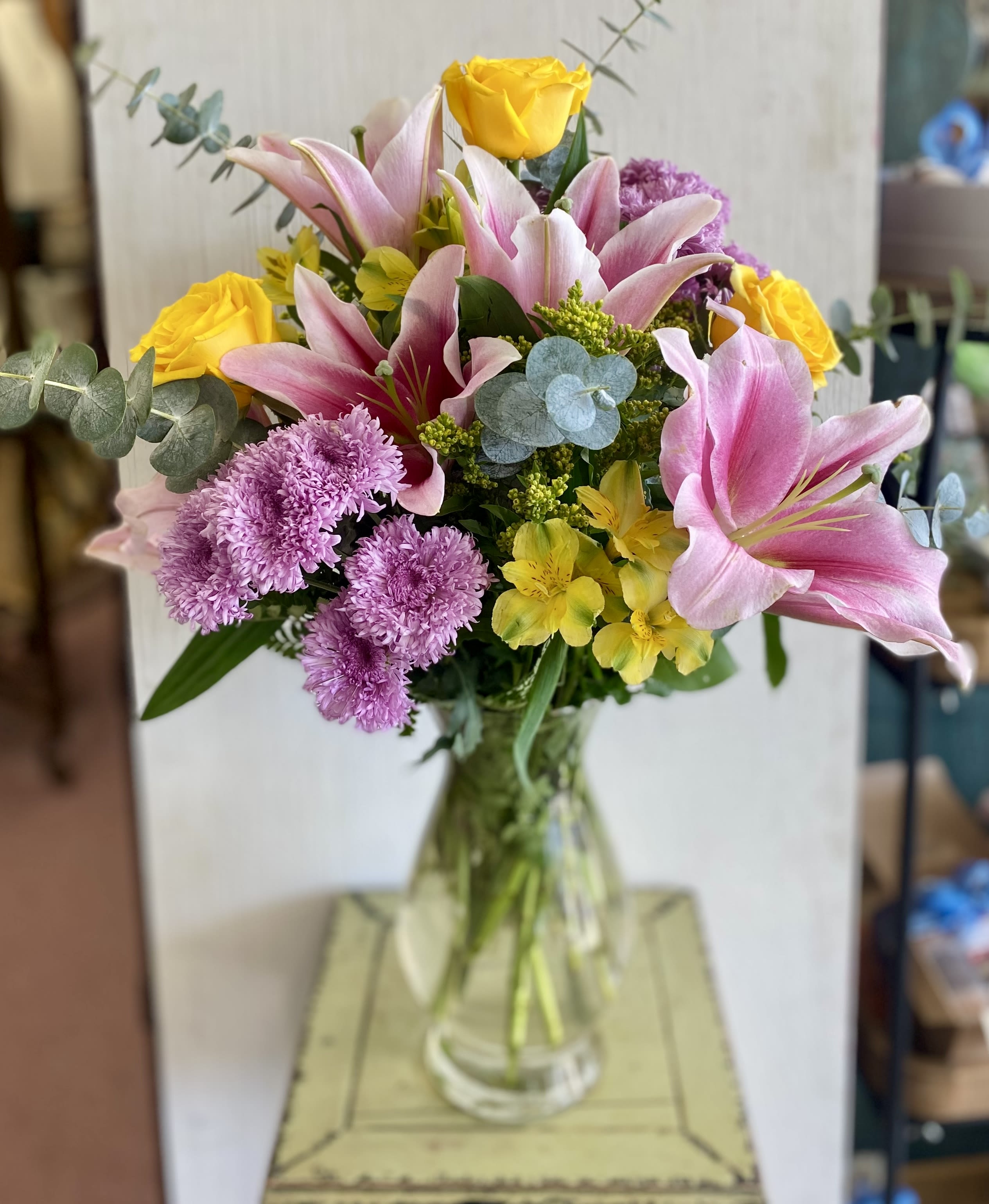 Bouquet of pink lilies, yellow roses, and purple flowers in a glass vase
