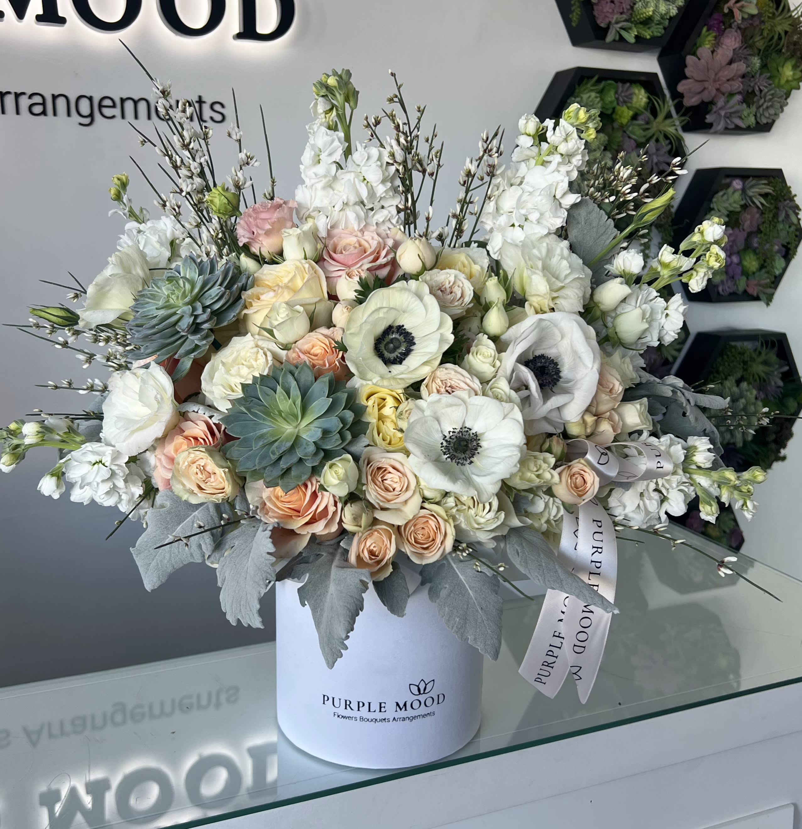 Peach Sorbet Box - Standard container size - D6.75'x H7.5' Deluxe container size - D8.25'x H9.5' Premium container size - D10.5'x H12.25'  The Peach Sorbet arrangement is a fresh and elegant mix of soft tones with a modern twist. Hints of peach, cream, and green create a refreshing palette that feels both luxurious and calming. Styled in a white box, it’s a true statement piece.  Key Features:     •    Elegant blend of peach, cream, and green shades     •    Includes modern touches with textured greenery     •    Presented in a sleek white box with ribbon detail     •    Perfect for housewarmings, celebrations, or chic gifting  Front side arrangement with lid in back. Box includes wet floral foam inside, box doesn't require vase.