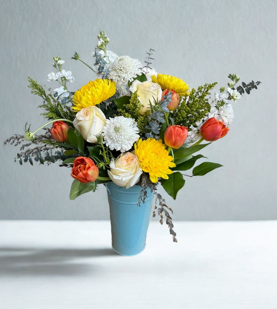 Sun &amp; Sky - "Sun &amp; Sky" is a bright, uplifting arrangement featuring golden blooms, soft ivory roses, and airy whites, accented with coral and fresh greenery. Designed in a cool blue vessel, it captures the warmth of sunlight against an open sky- cheerful, fresh, and full of light. 