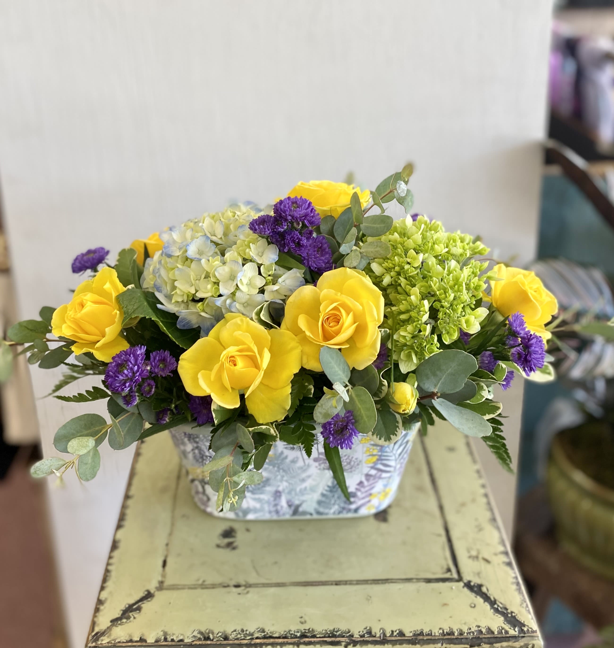 Yellow roses and purple flowers in a patterned rectangular container