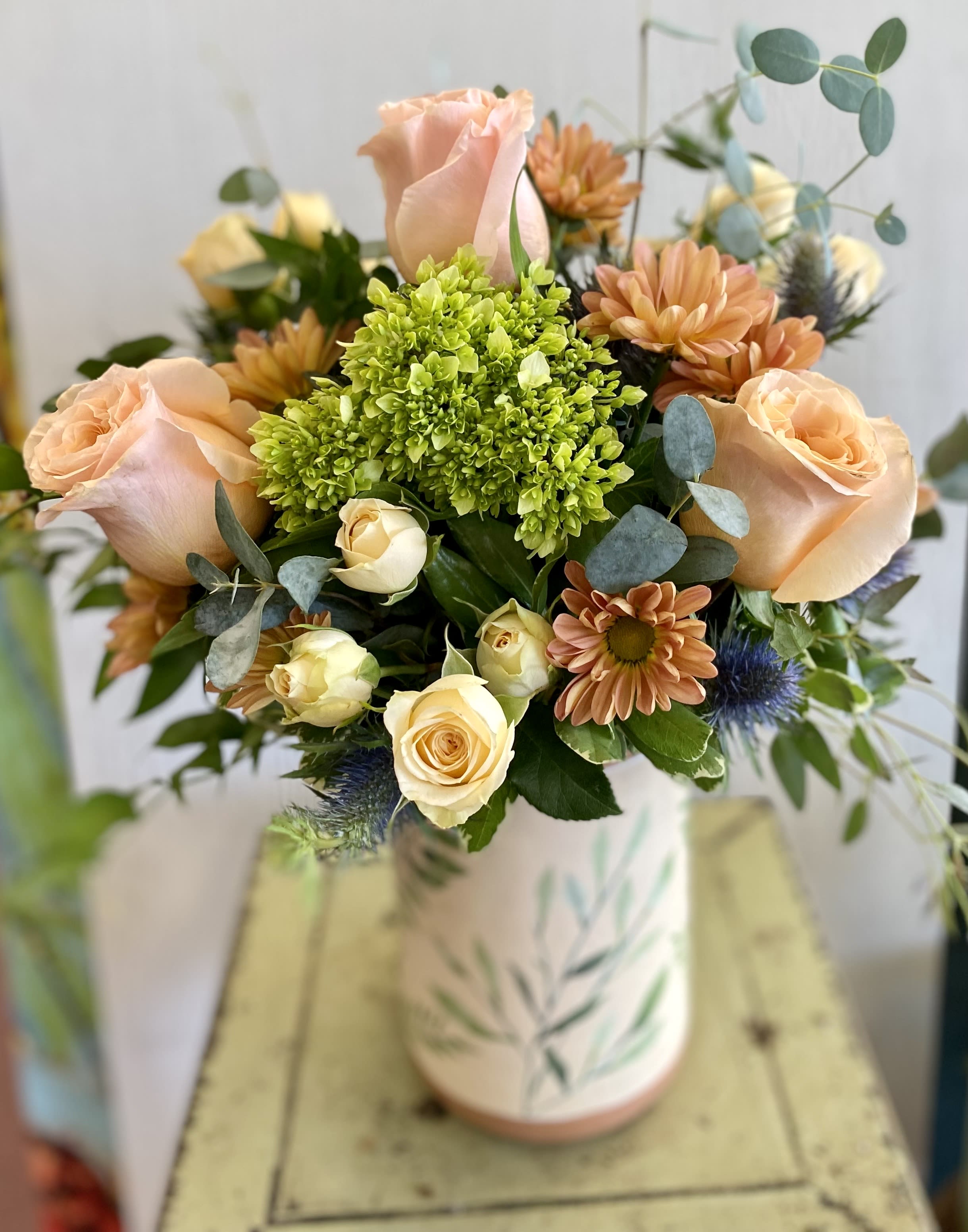 Peach roses and orange daisies in a patterned vase