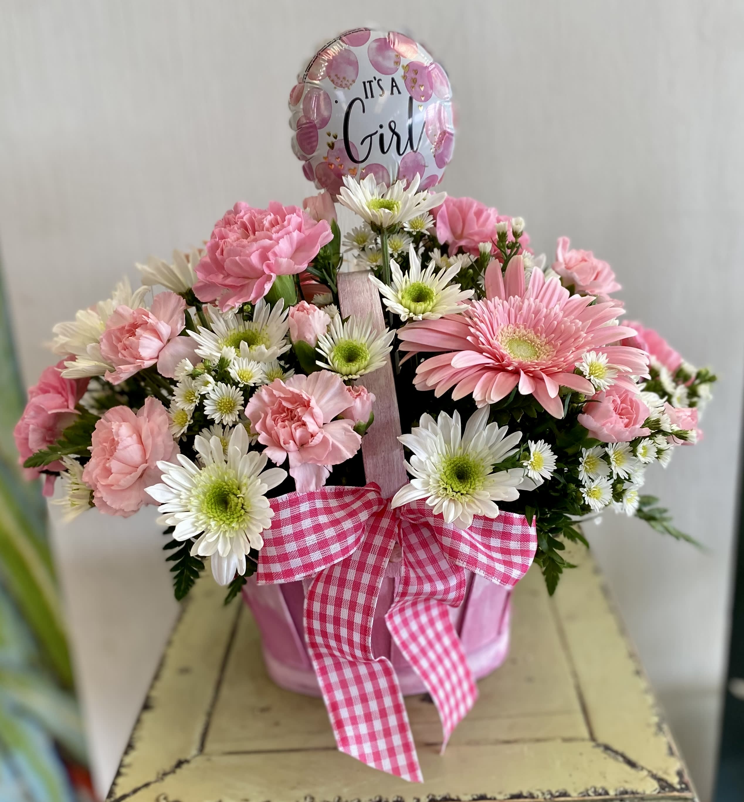 Pink and white flower arrangement in a pink container with a "It's a Girl" balloon