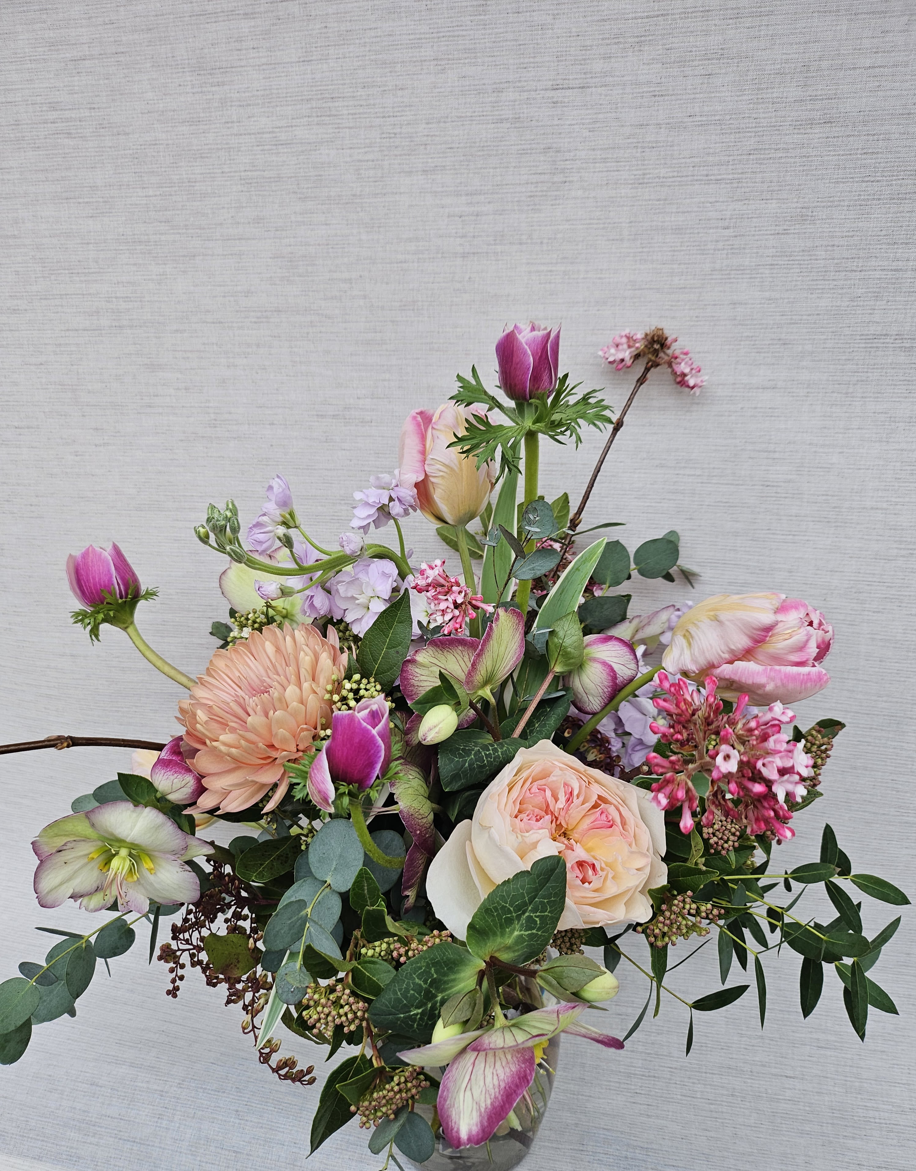Loose arrangement of pink and peach blooms, including roses and tulips, in a clear glass vase