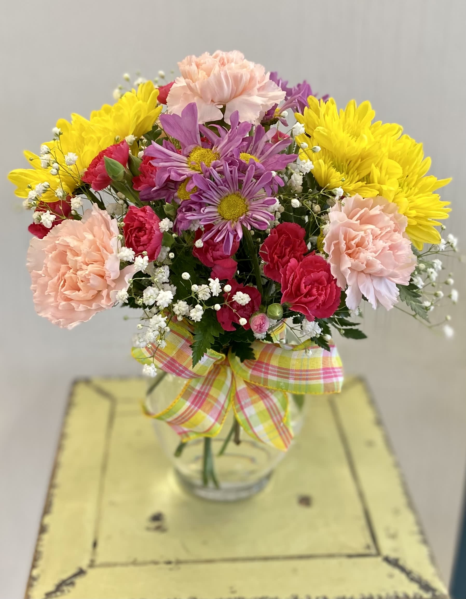Colorful bouquet of carnations and daisies in a glass vase with a plaid ribbon