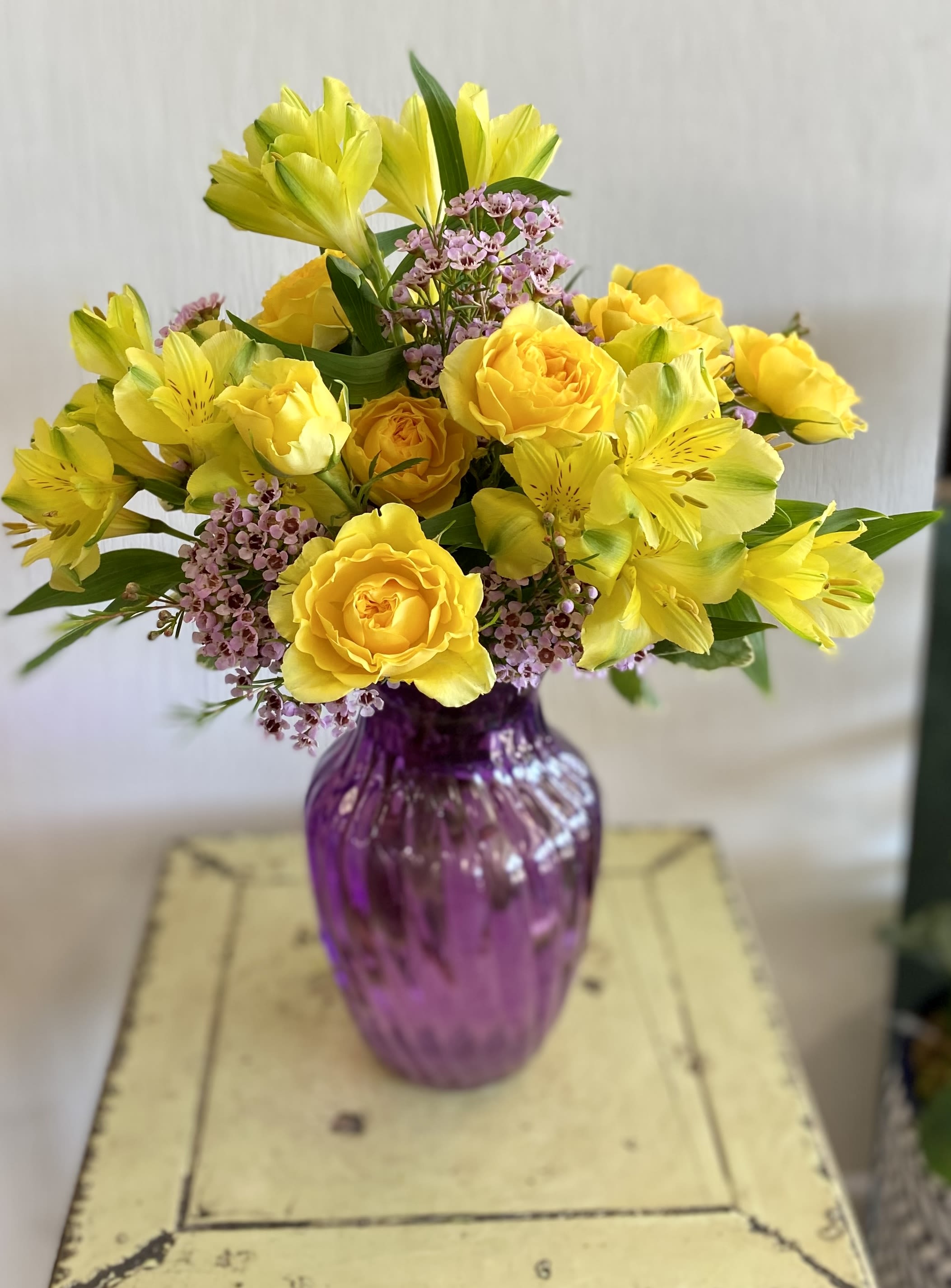 Yellow roses and alstroemeria in a purple glass vase
