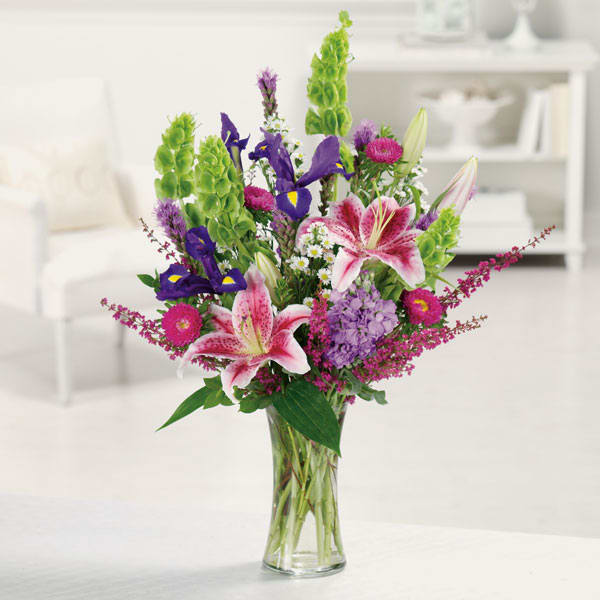 Mixed bouquet of lilies, irises, and purple flowers in a glass vase