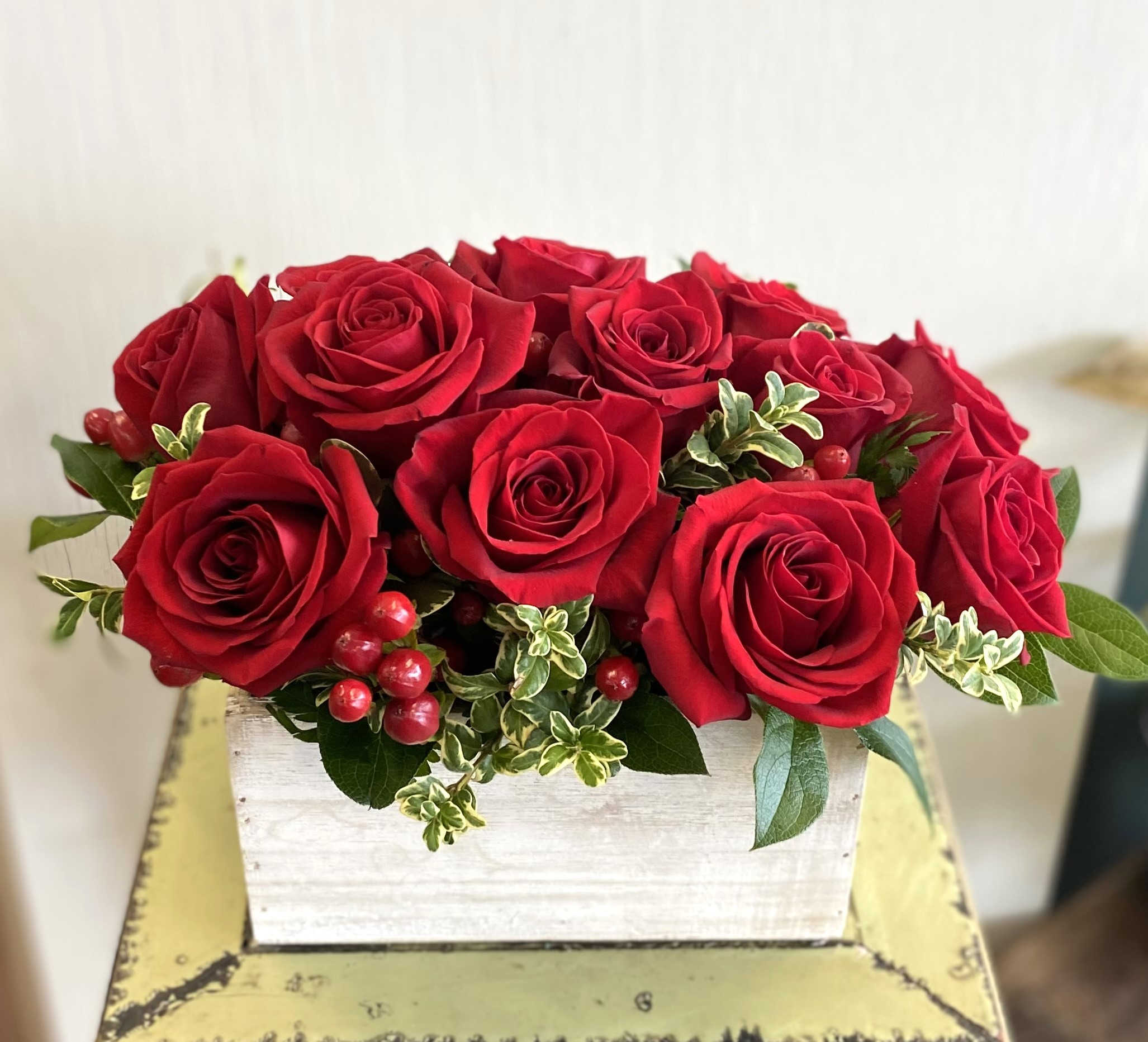Red roses arranged in a white wooden box with berries and greenery